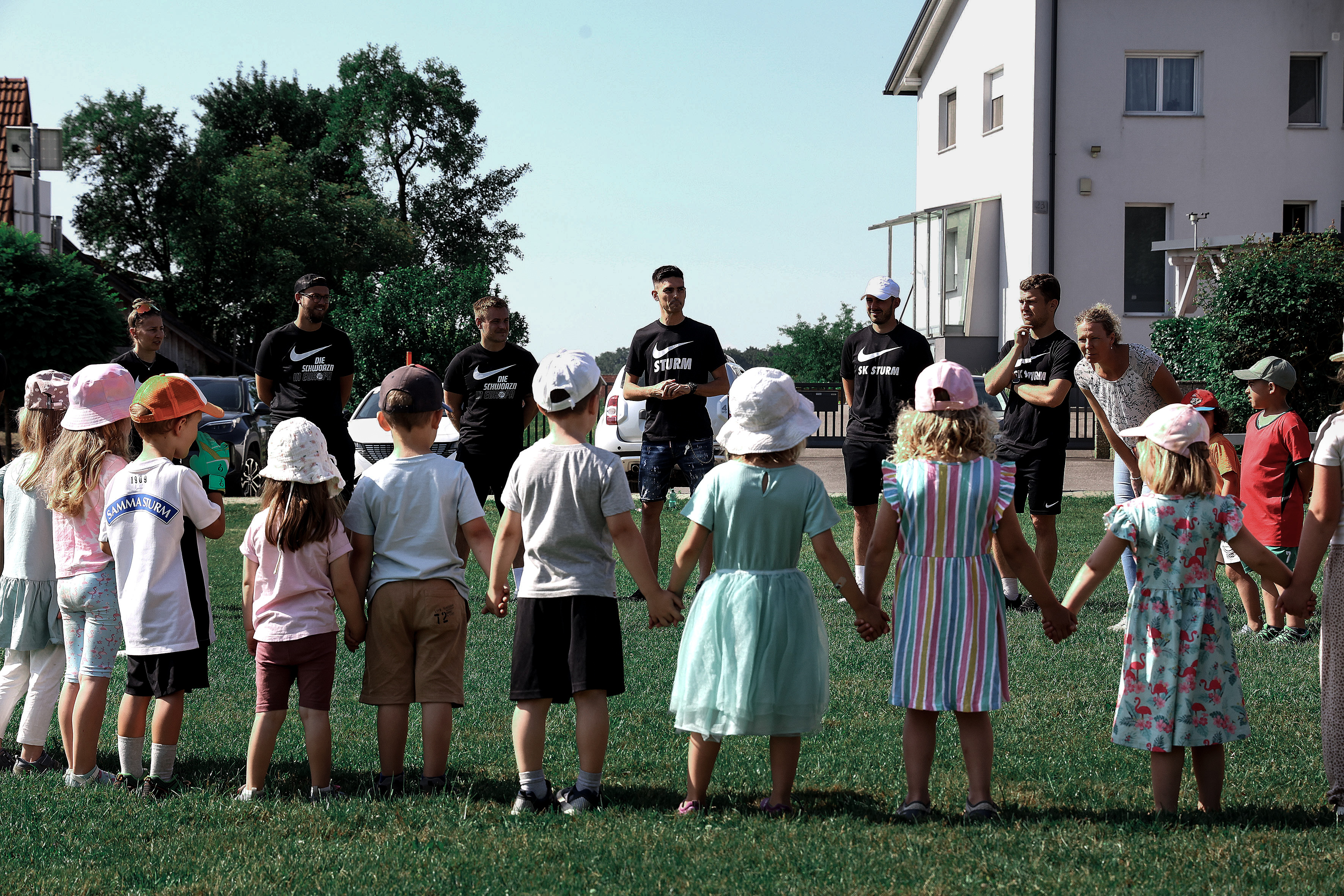 Ein Kreis mit Kinder geben sich die Hand und schauen auf sieben Erwachsene
