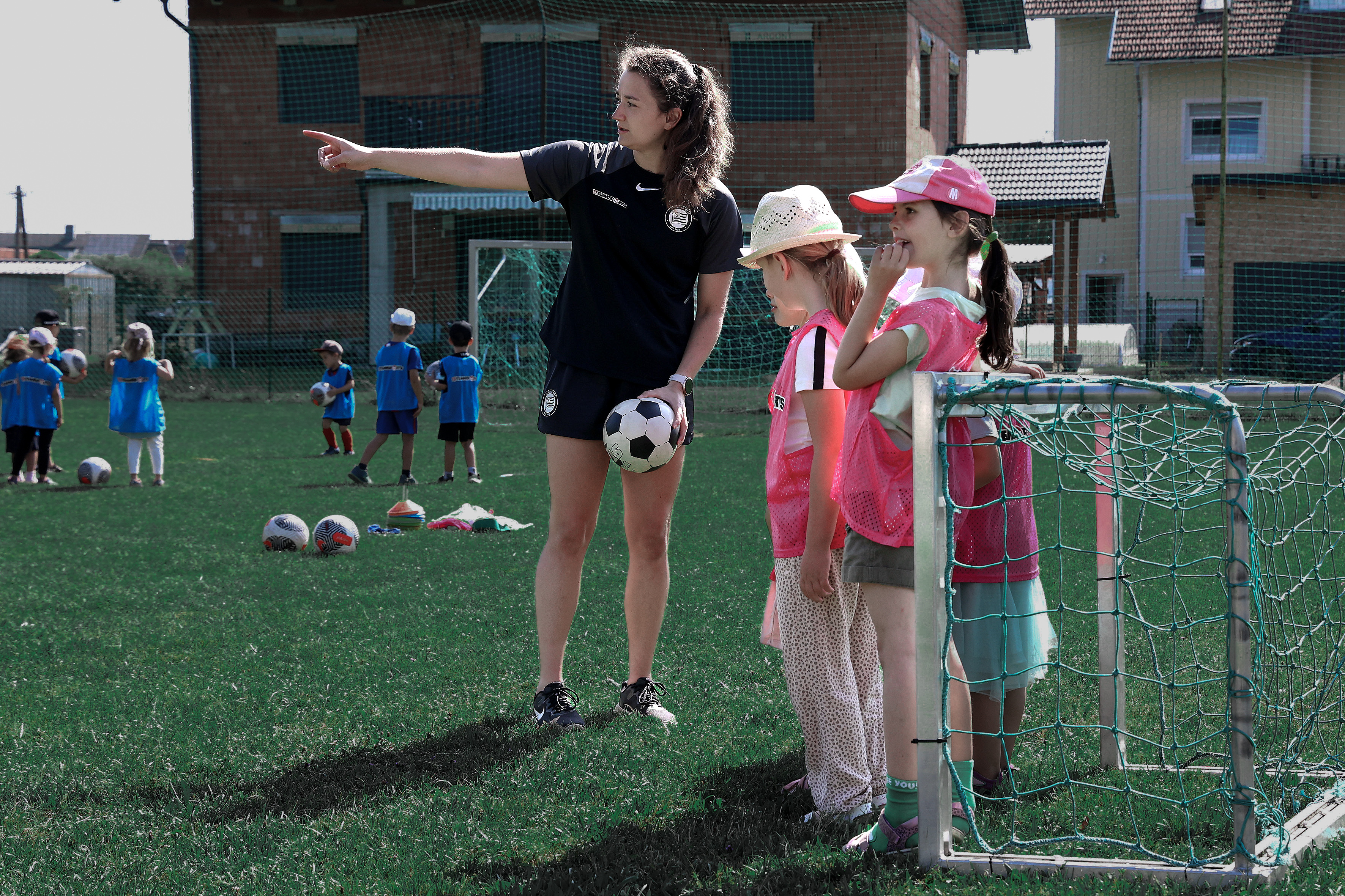 Frau mit Ball zeigt Kindern etwas in der Ferne