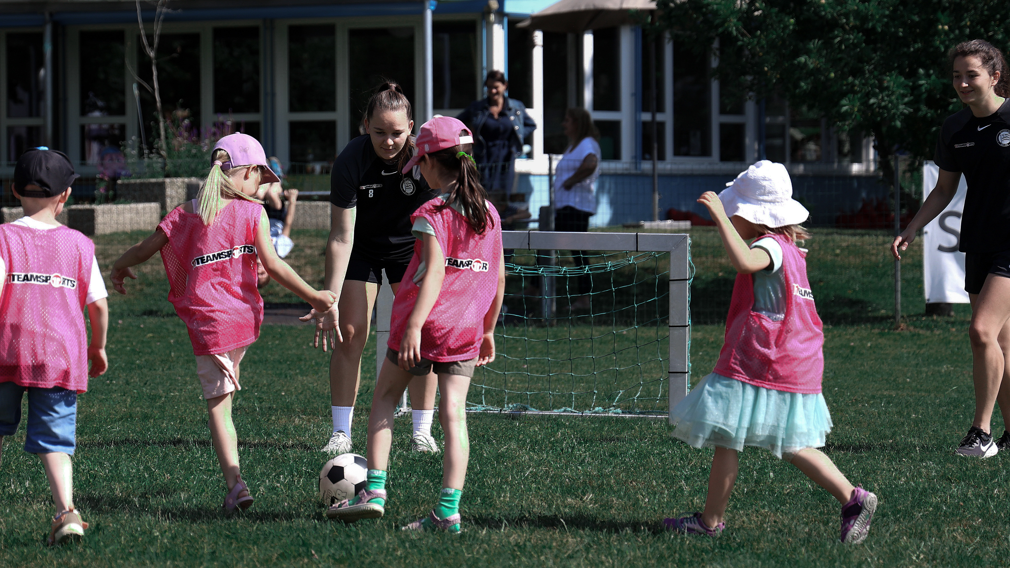 Zwei erwachsene Frauen spielen Fußball mit vier Kindern