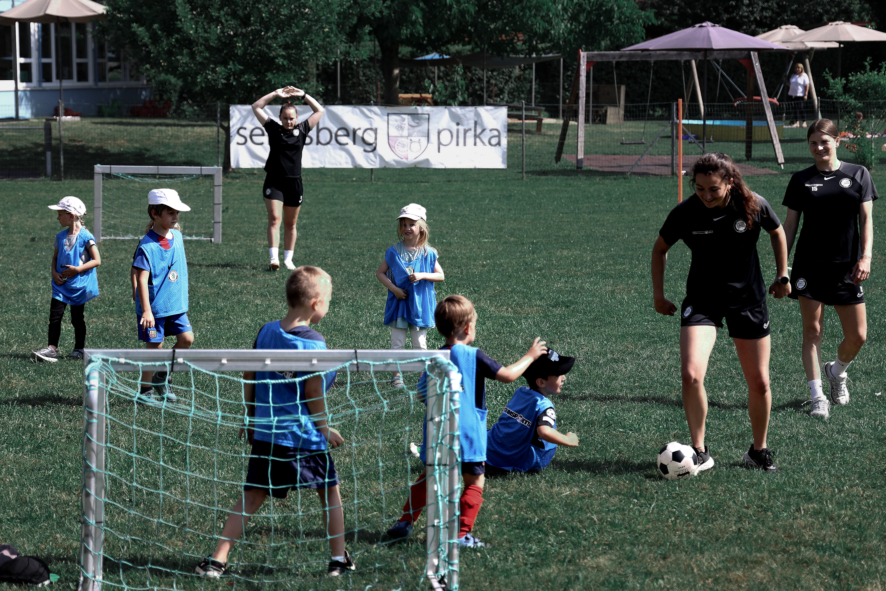 Drei Frauen spielen mit sechs Kindern Fußball