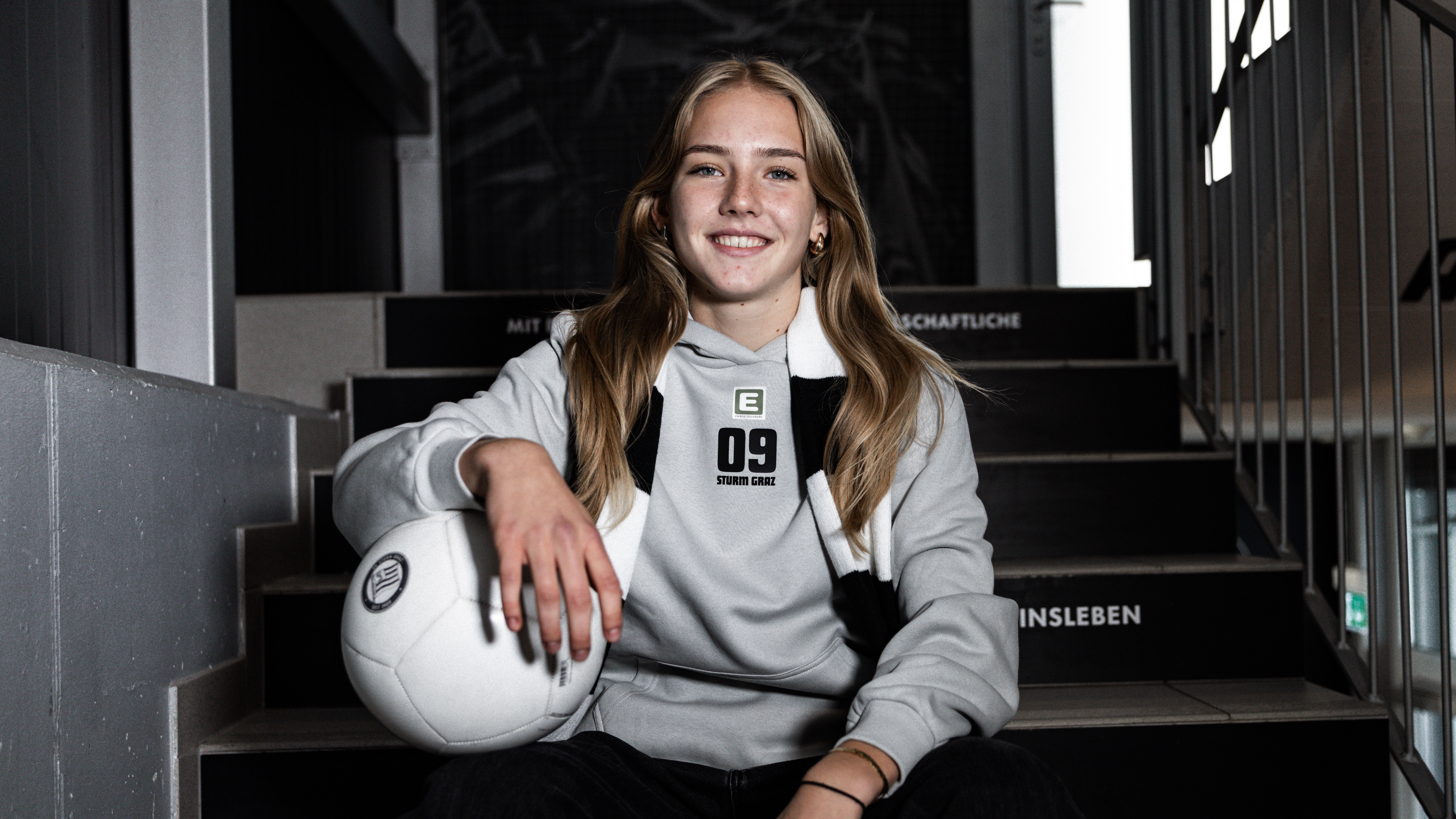 Eine Frau mit Schal und Ball sitzt auf einer Stiege