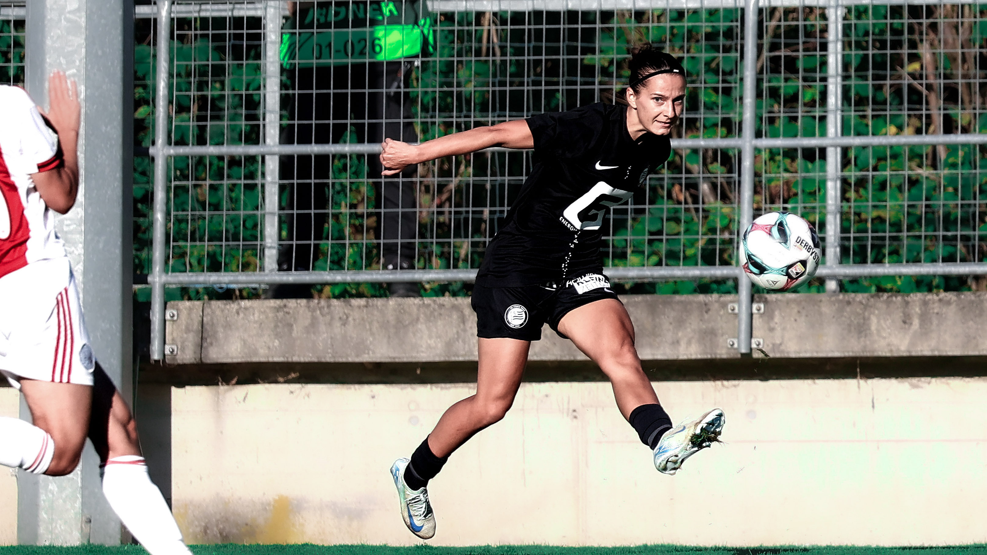 Eine Spielerin im schwarzen Trikot schießt den Ball mit ihrem linken Fuß.