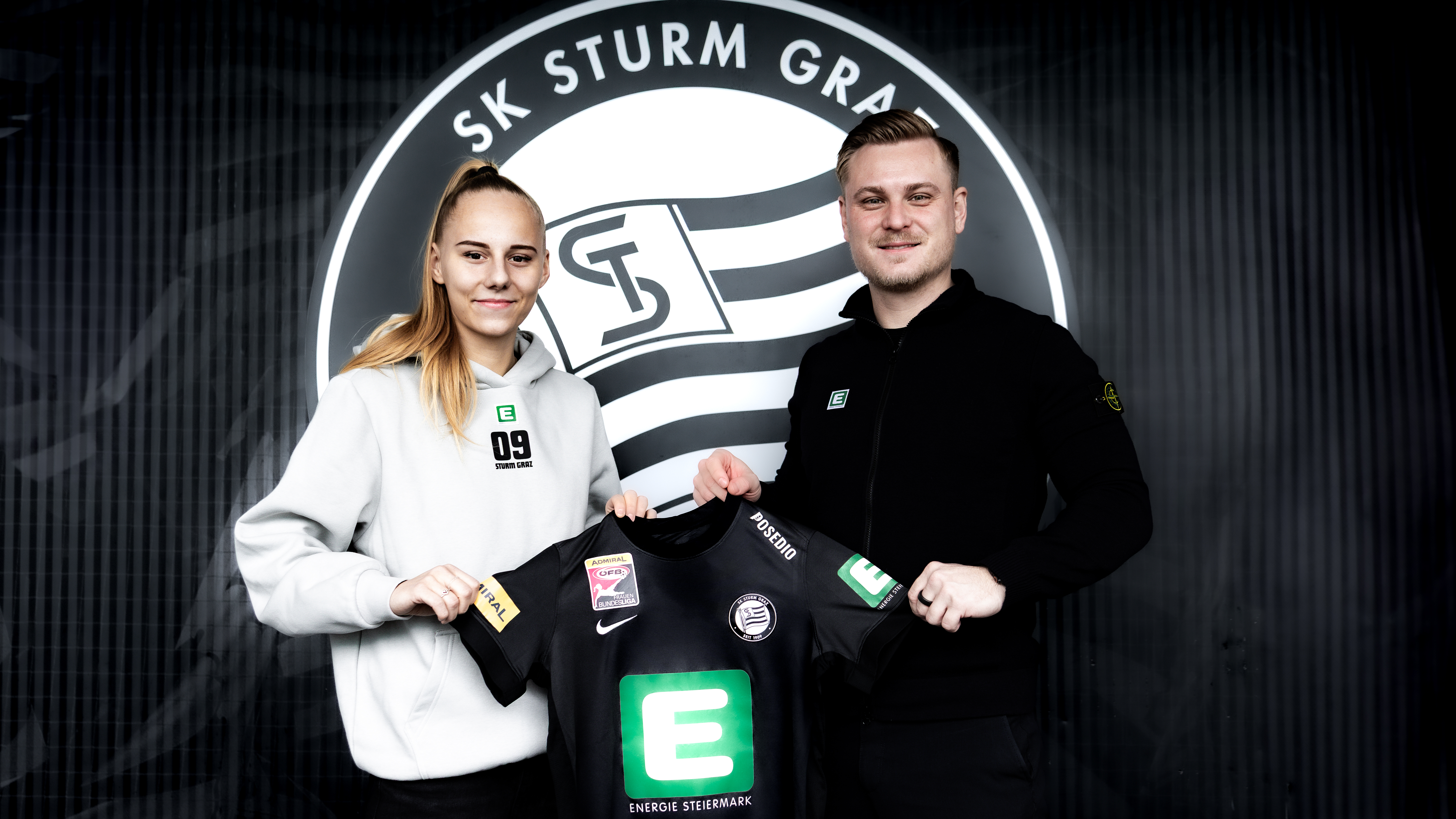 Ein Mann und eine Frau halten ein schwarzes Trikot in der Hand