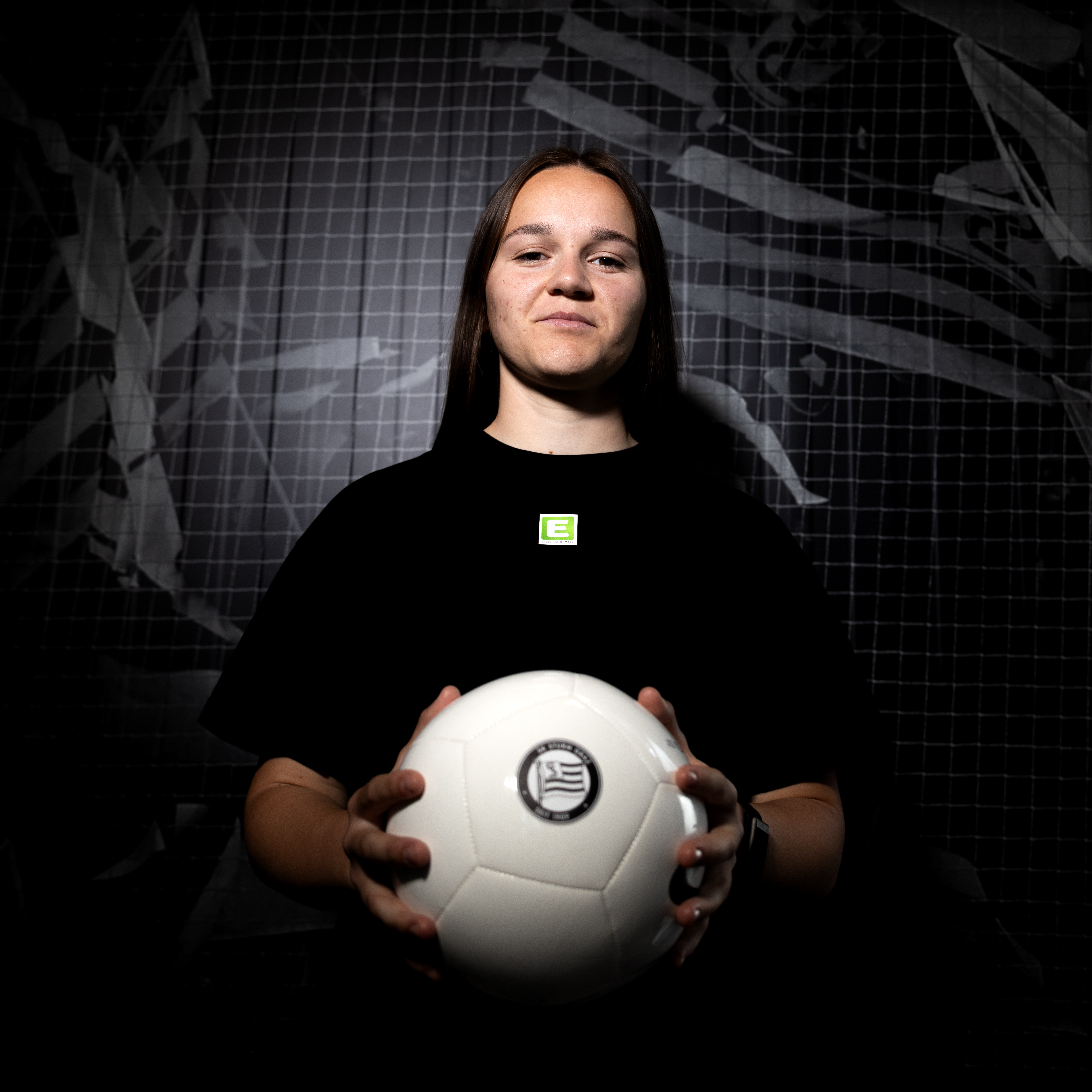 Eine Frau in schwarzem Shirt hält einen weißen Ball und lächelt.
