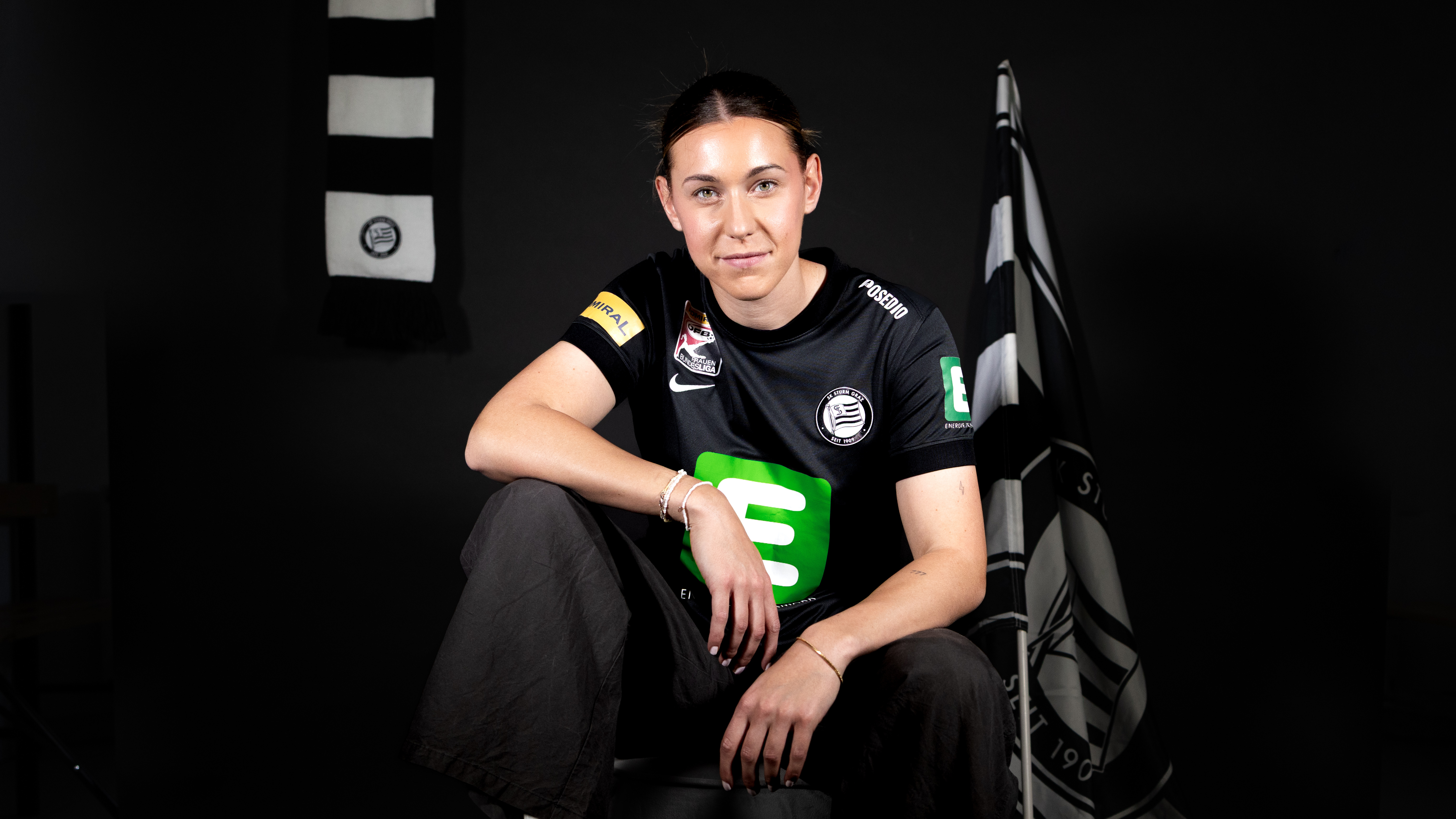 Eine Frau in schwarzem Trikot sitzt auf einem Stuhl und lächelt.