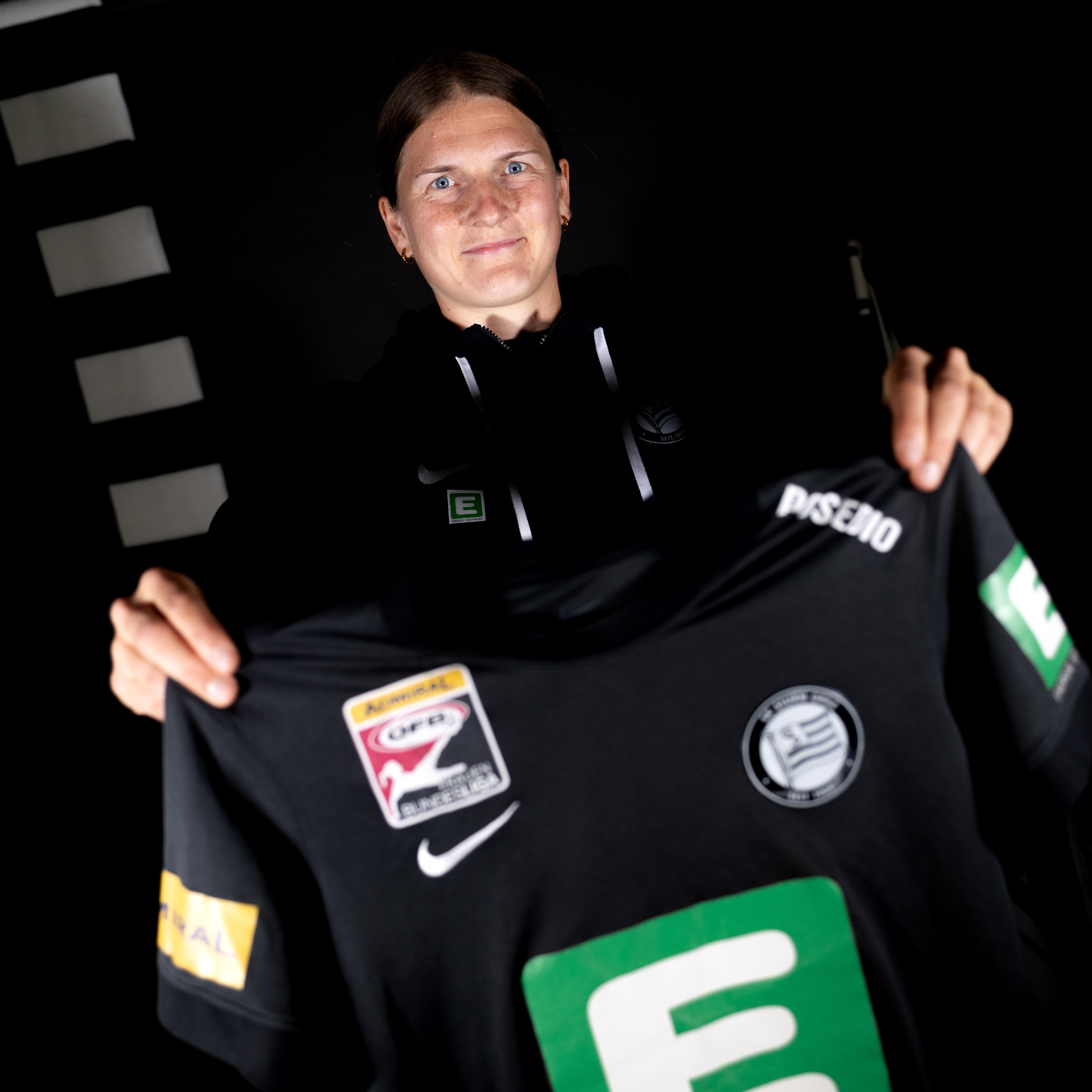 Eine Frau hält ein Trikot in die und lächelt.