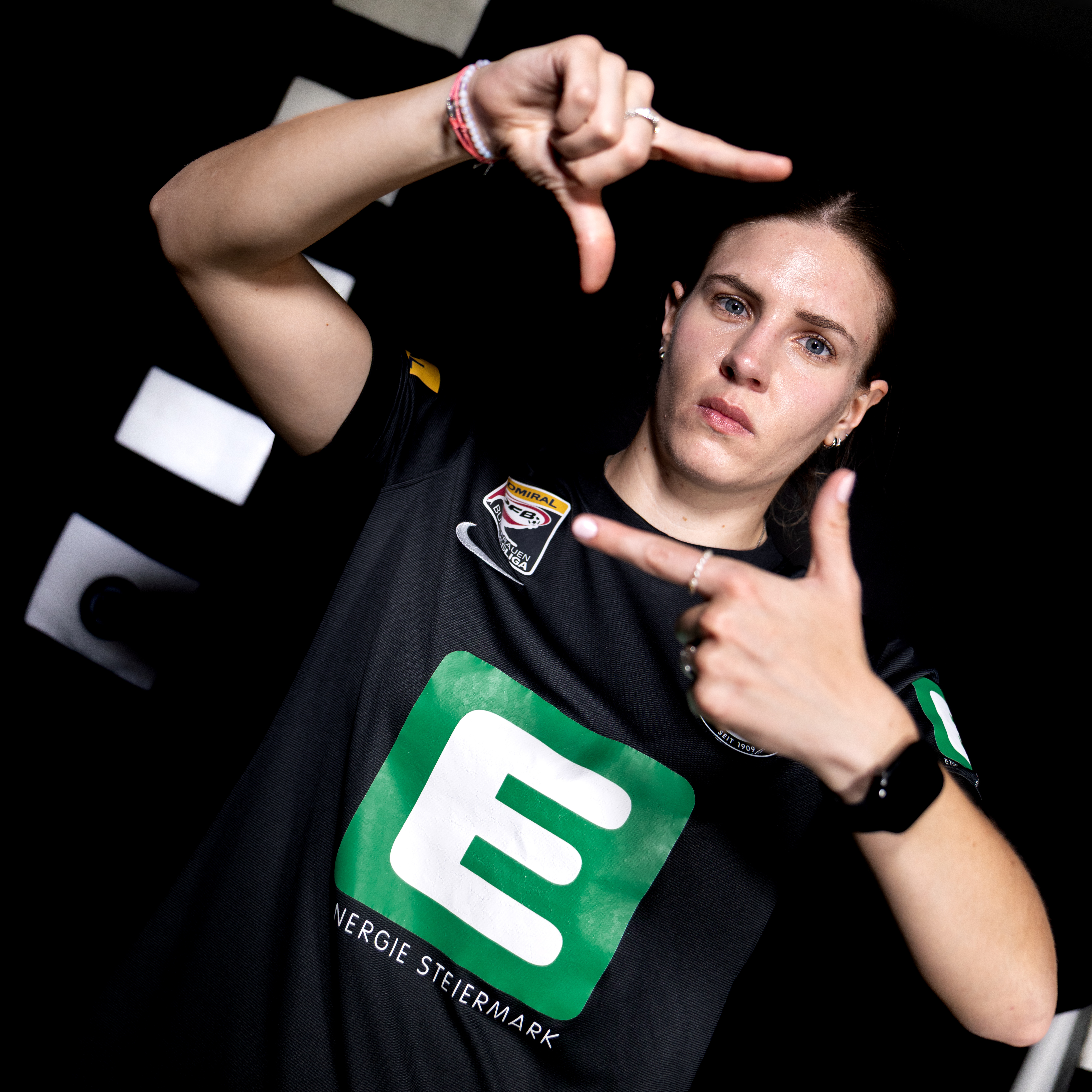 Eine Frau in schwarzem Trikot zeigt ein Viereck in die Kamera und schaut konzentriert.