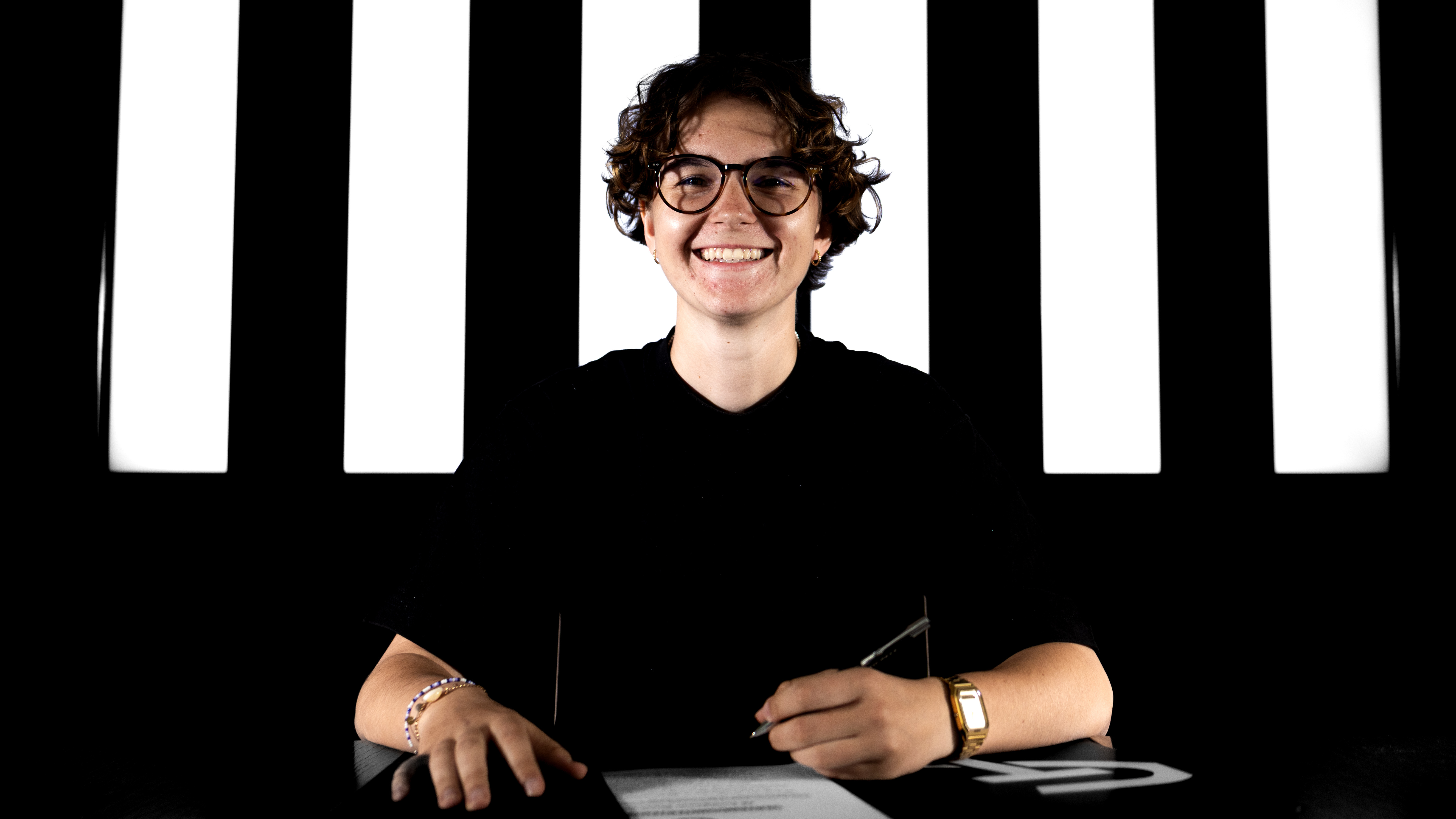 Eine Frau in schwarzem Shirt hält einen Stift und lächelt.