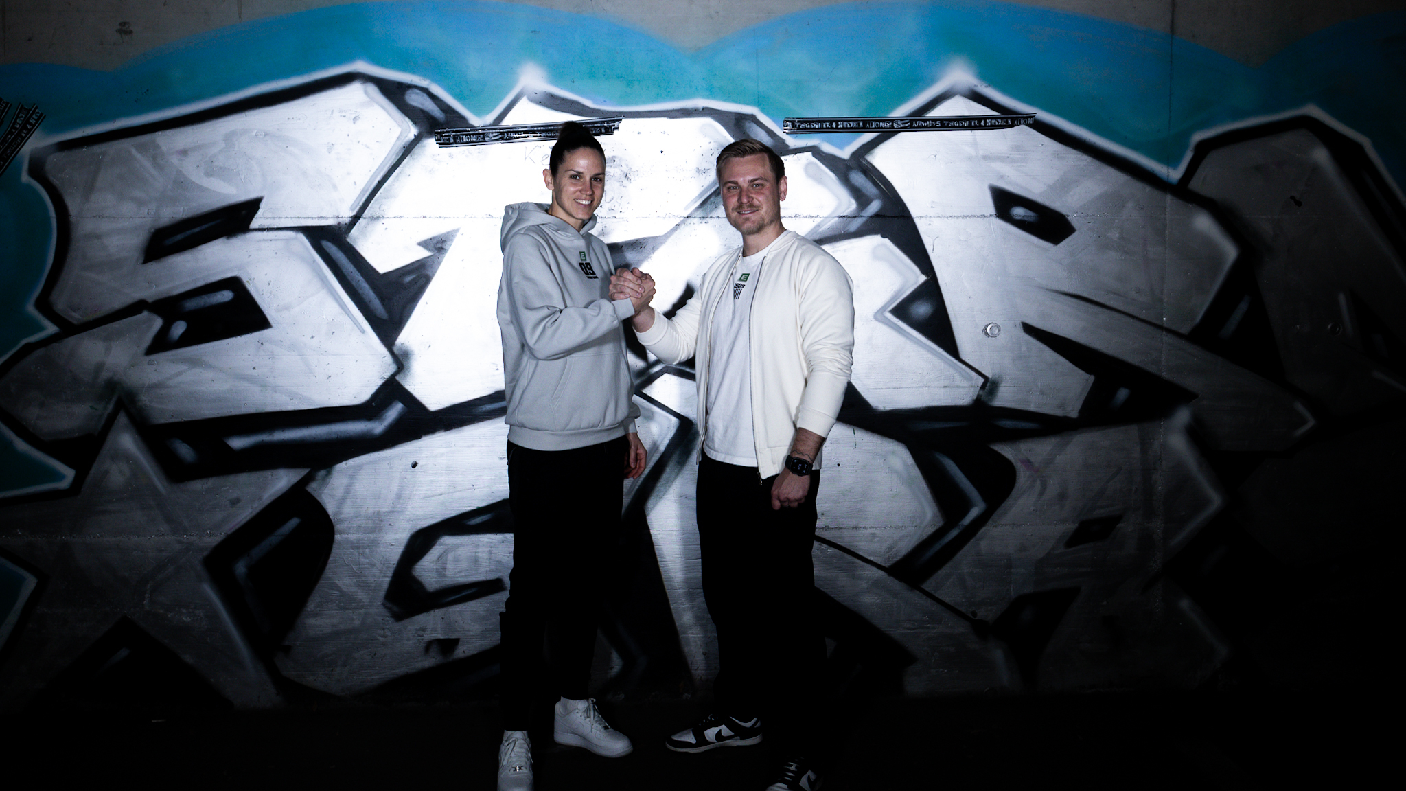 Ein Mann und eine Frau klatschen vor einem Graffiti ein.