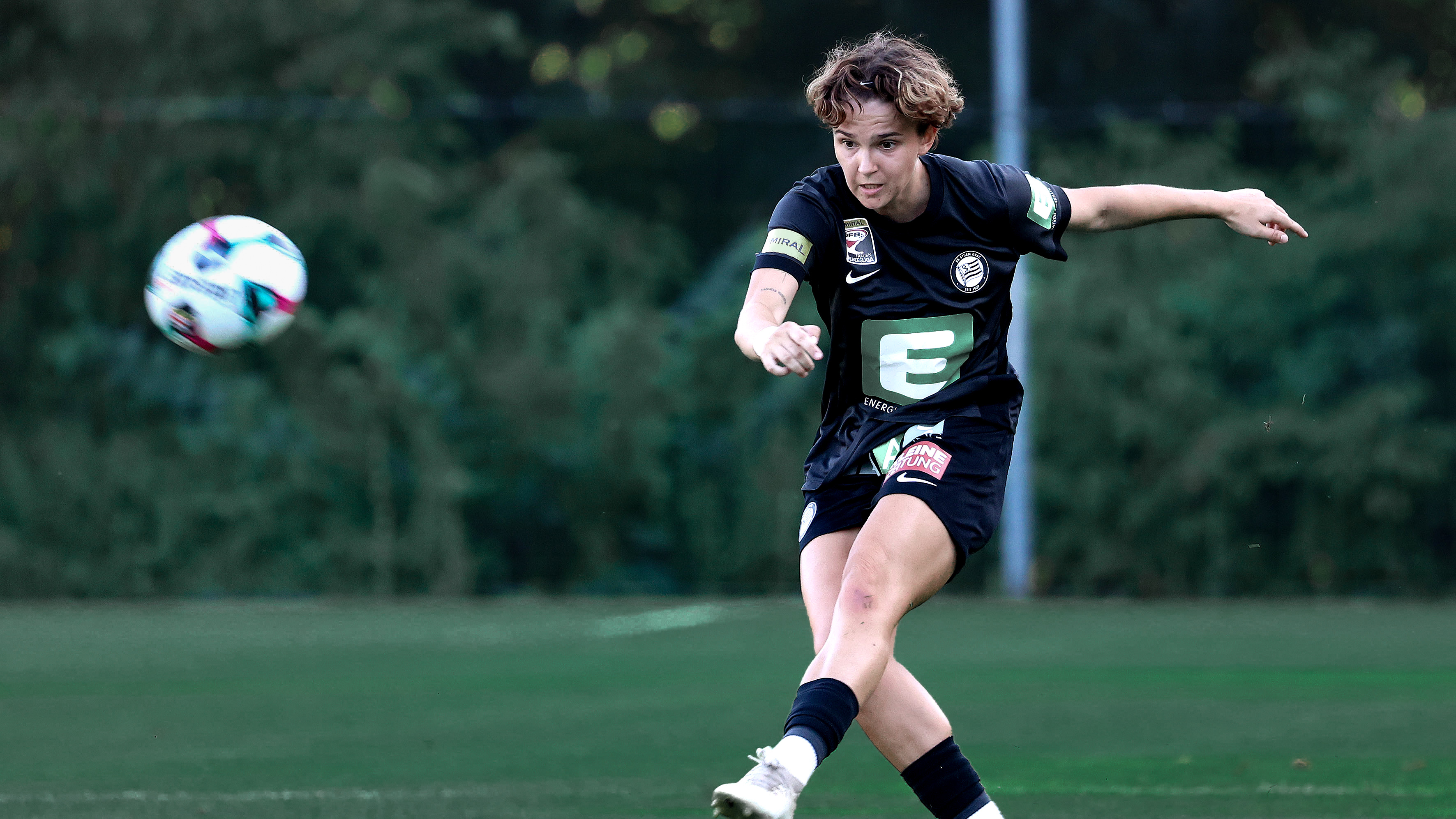 Fußballspielerin in schwarzem Trikot schießt den Ball weg.