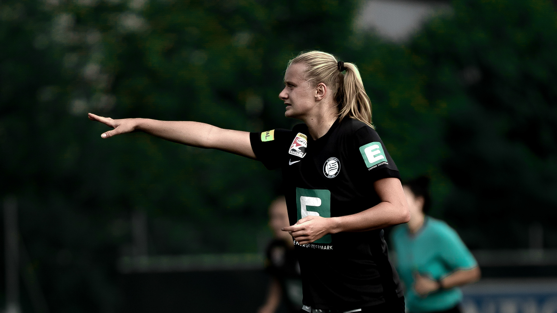 Eine Frau in schwarzem Trikot zeigt in eine Richtung.