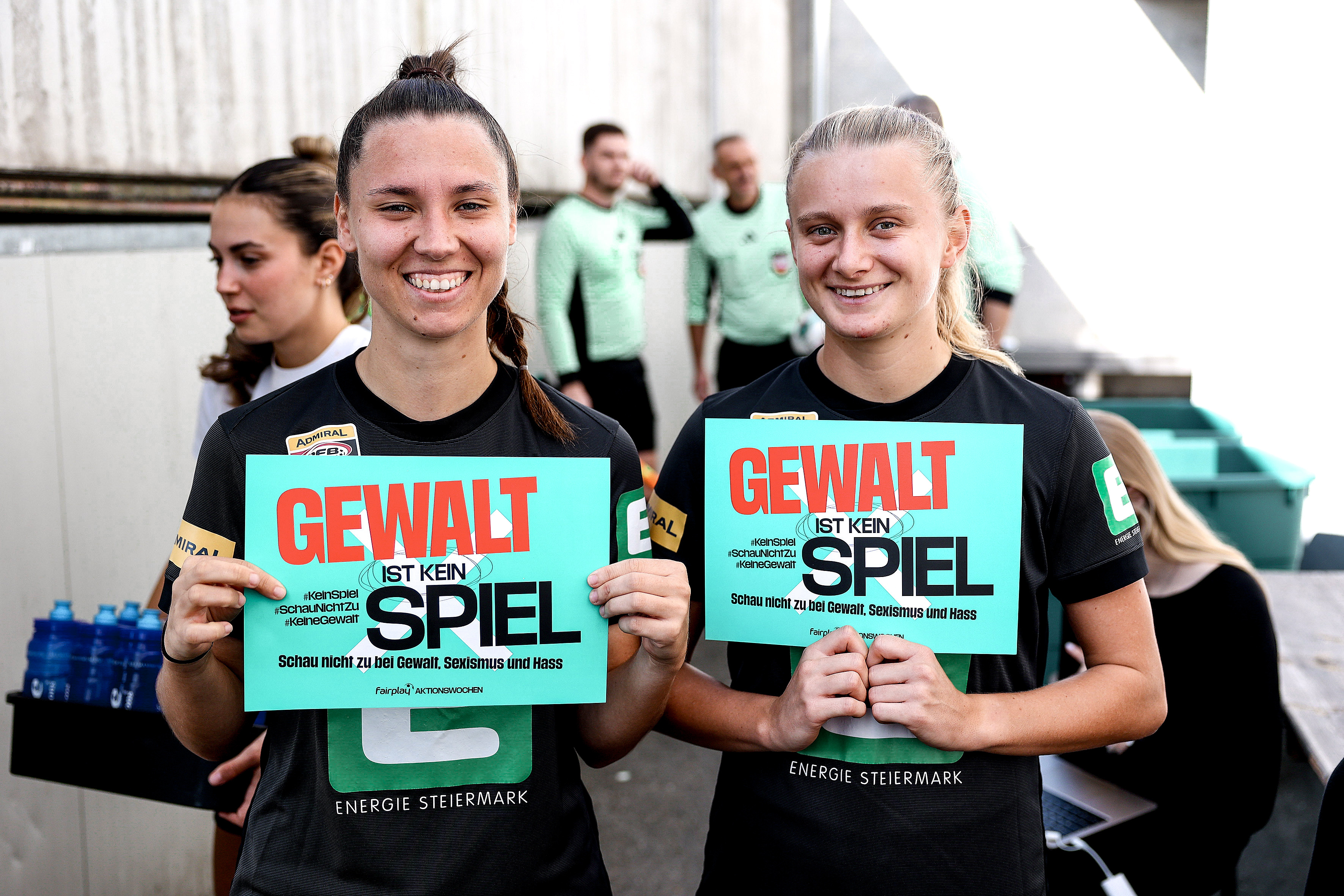 Zwei Frauen halten zwei Schilder in die Kamera.