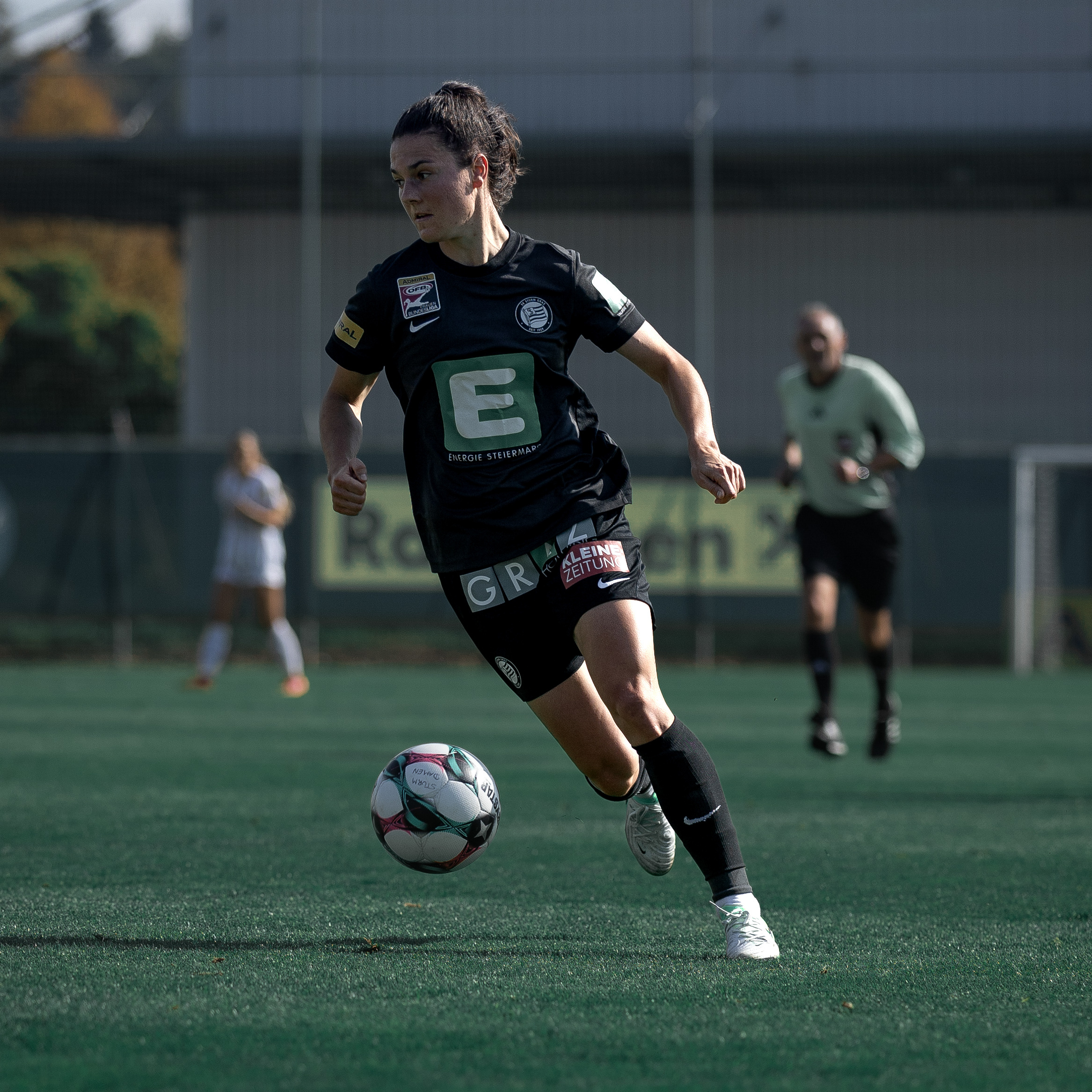 Eine Frau im schwarzen Trikot hat den Ball und schaut in die ferne.