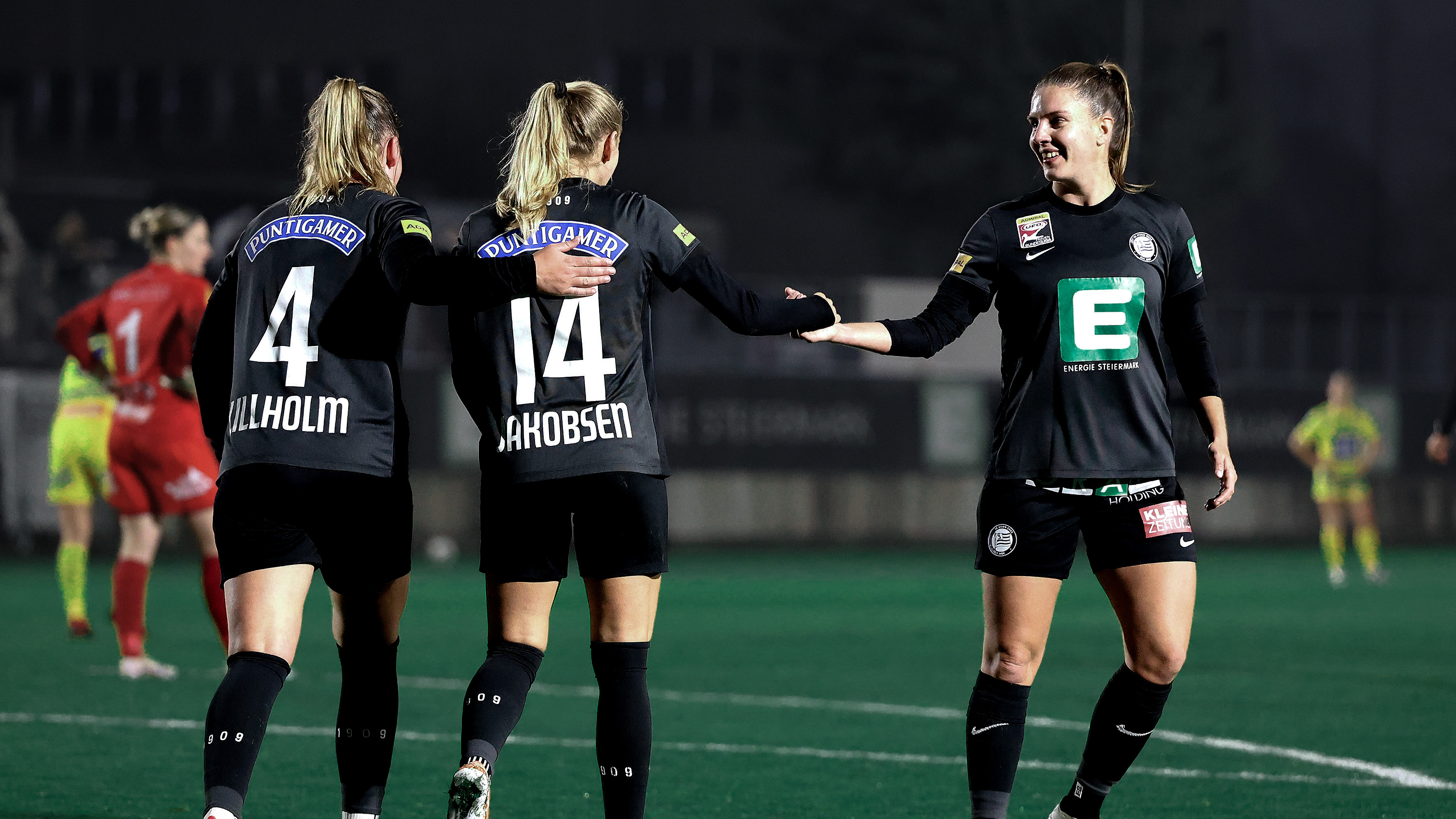 Drei Frauen in schwarzem Trikot feiern gemeinsam und freuen sich.