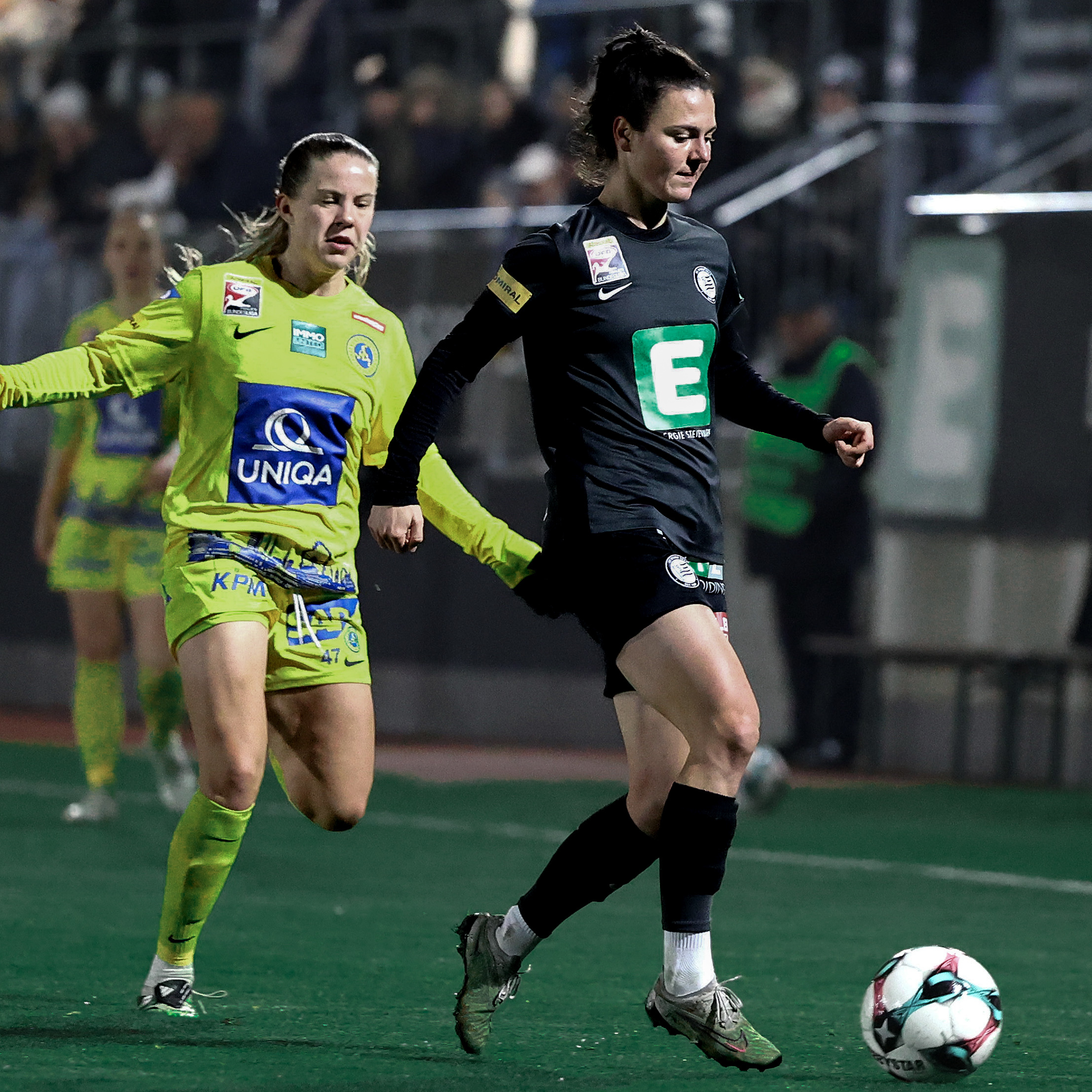 Eine Frau in schwarzem Trikot und eine Frau in einem gelben Trikot schauen beiden auf den Ball.