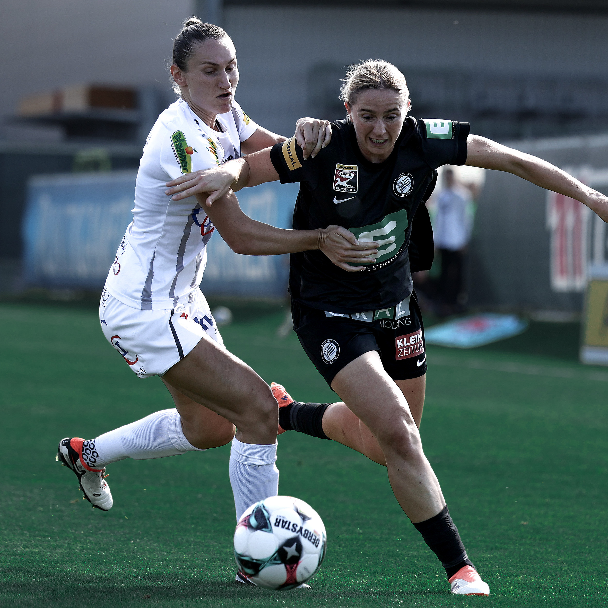 Eine Frau in schwarzem Trikot und eine Frau mit weißem Trikot führen einen Zweikampf.