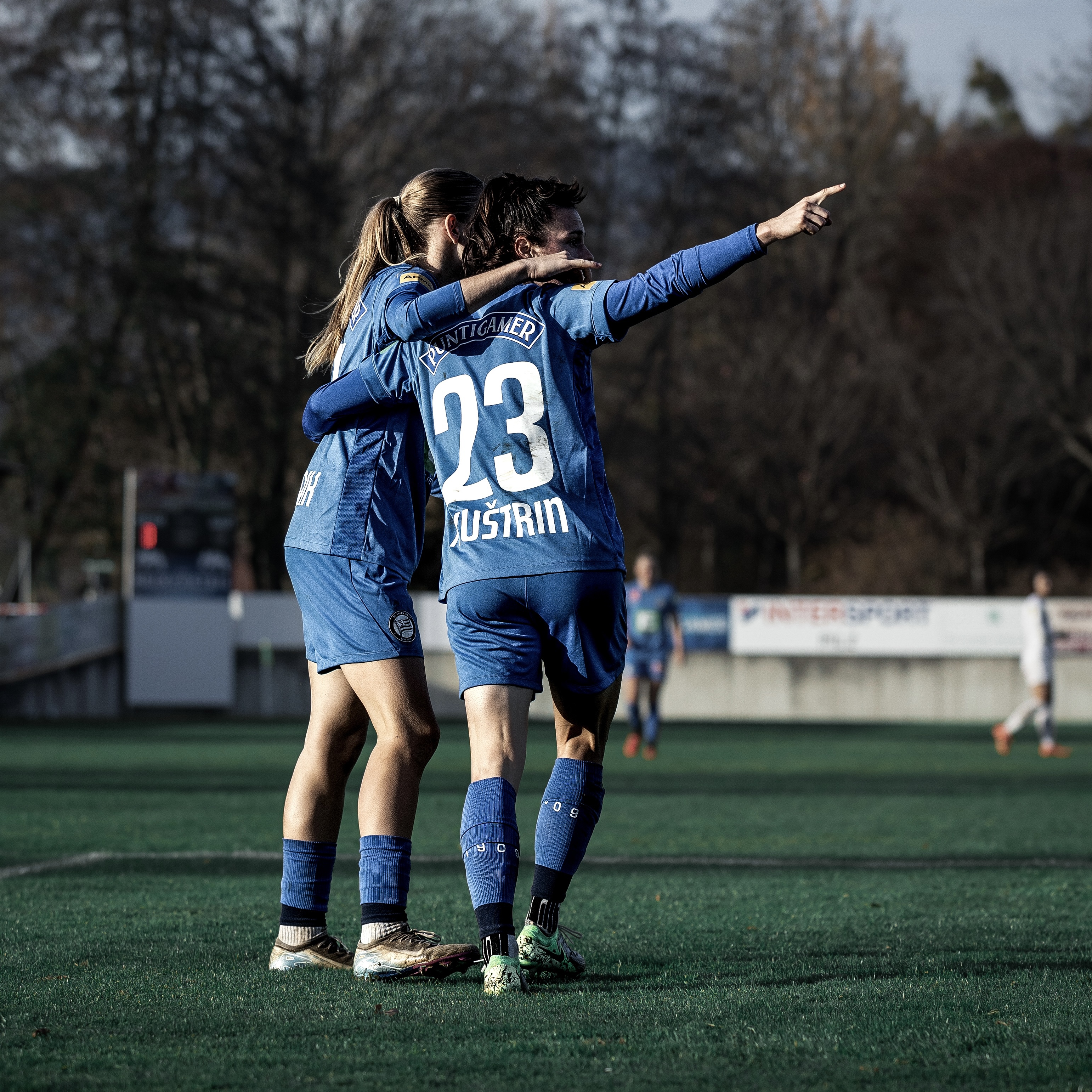 Zwei Frauen in blauen Trikots jubeln gemeinsam, die rechte Frau hebt die rechte Hand.