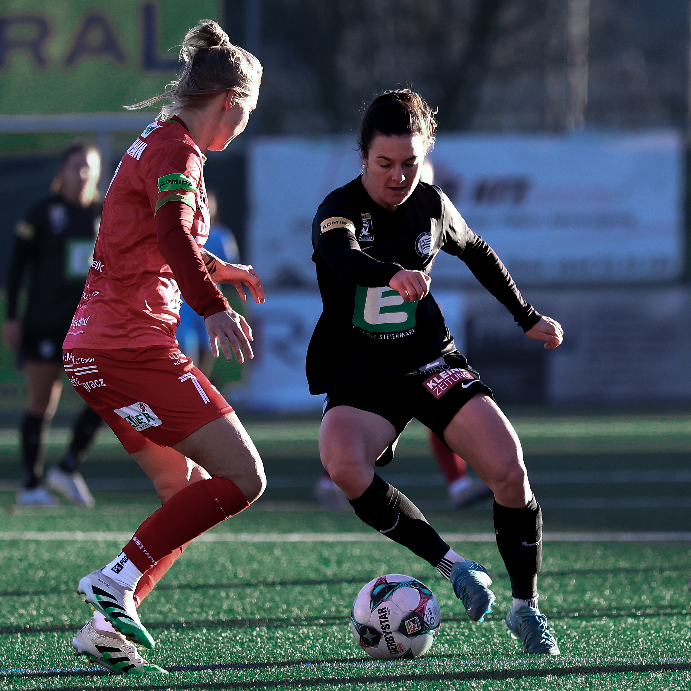 Eine Frau in schwarzem Trikot hat den Ball und eine Frau in rotem Trikot probiert den Ball zu bekommen.