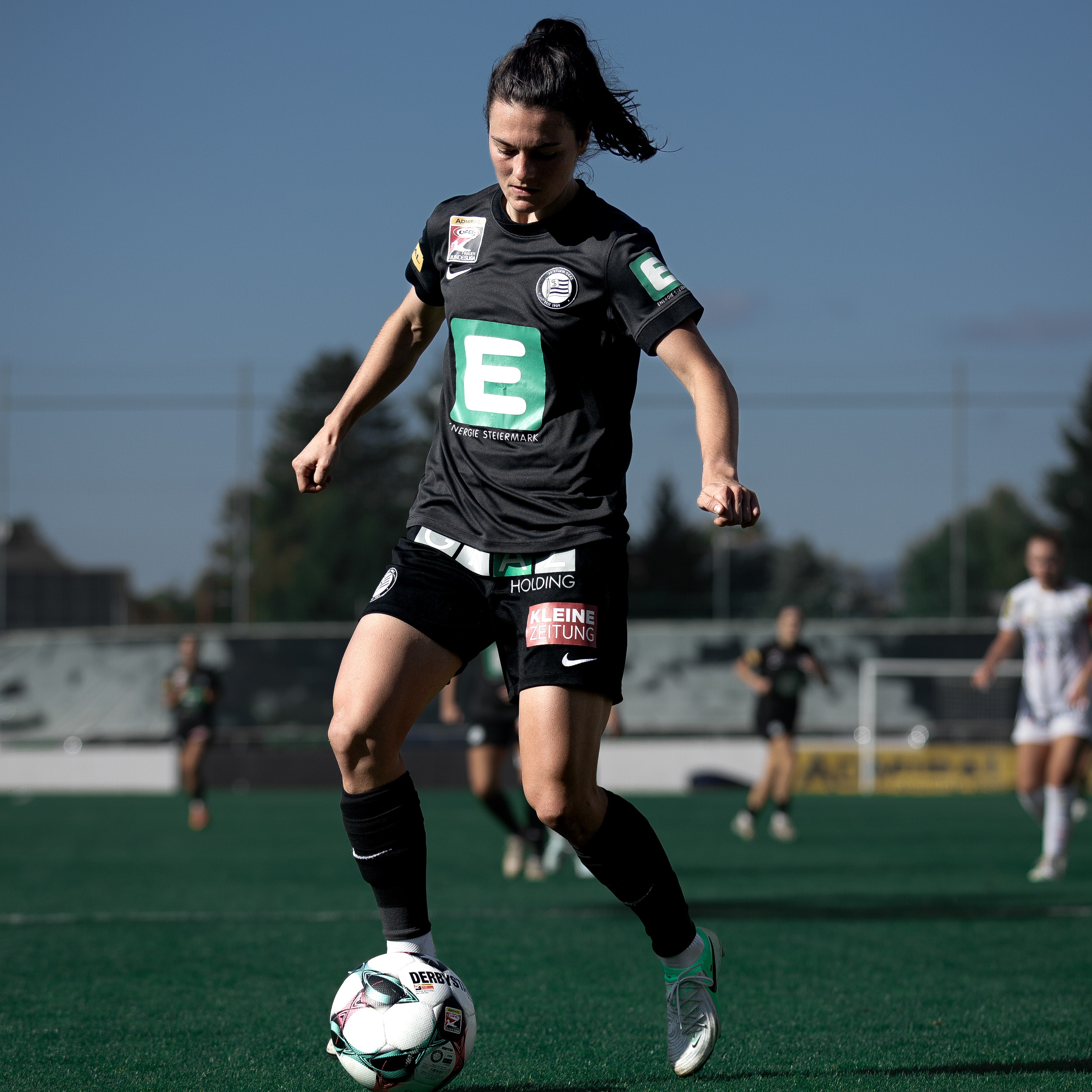 Eine Frau in schwarzem Dress hat einen Ball am Fuß und sieht in konzentriert an.