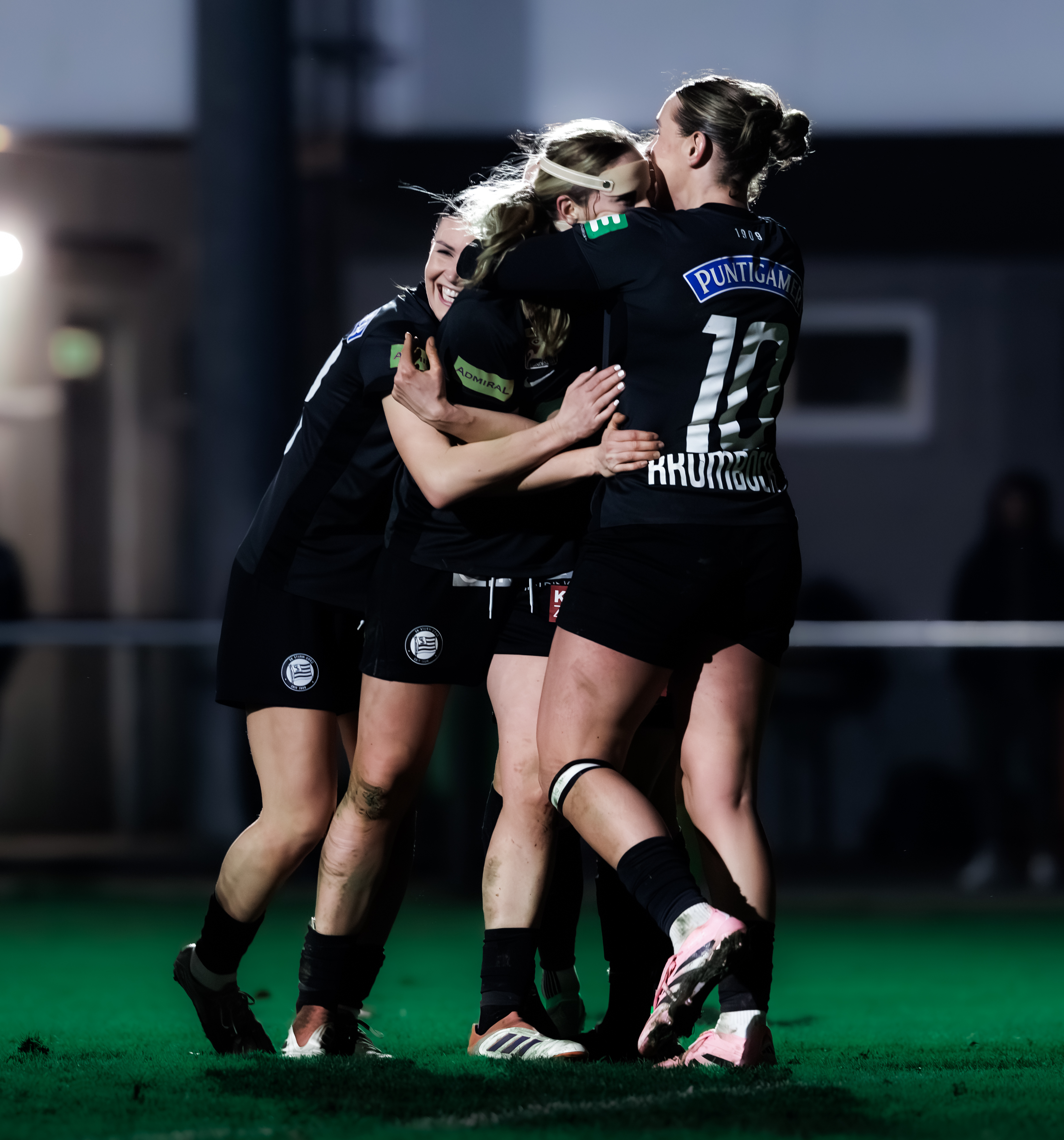 Drei Damen mit schwarzen Trikots jubeln gemeinsam.