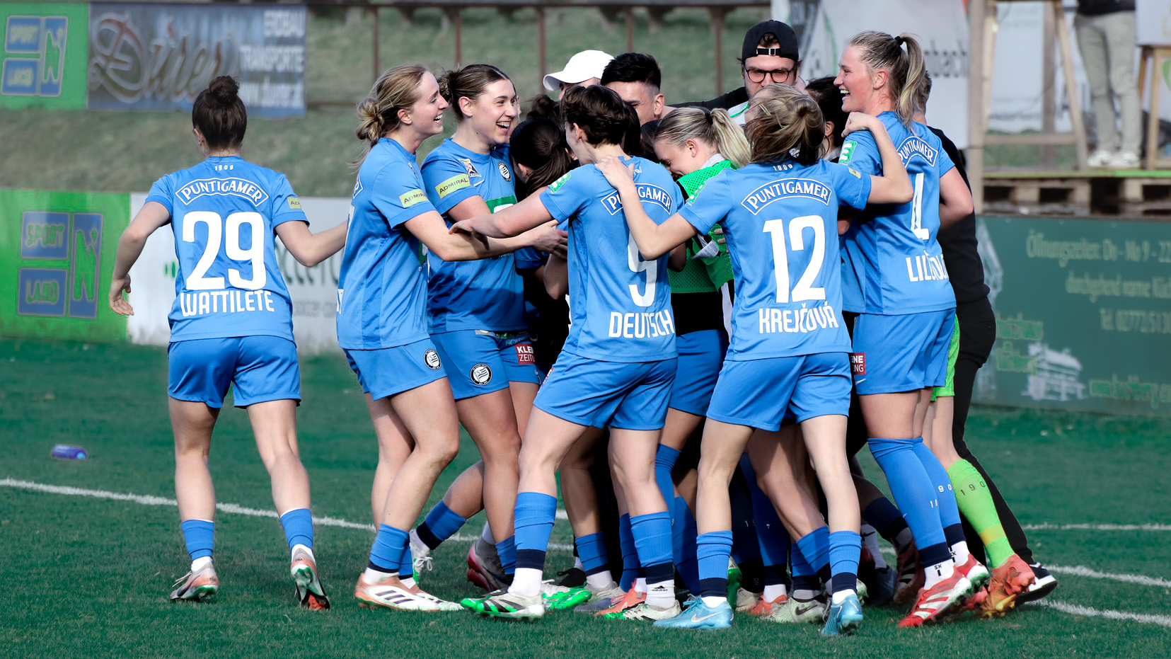 Mehrere Frauen in blauen Trikots umarmen sich und freuen sich.