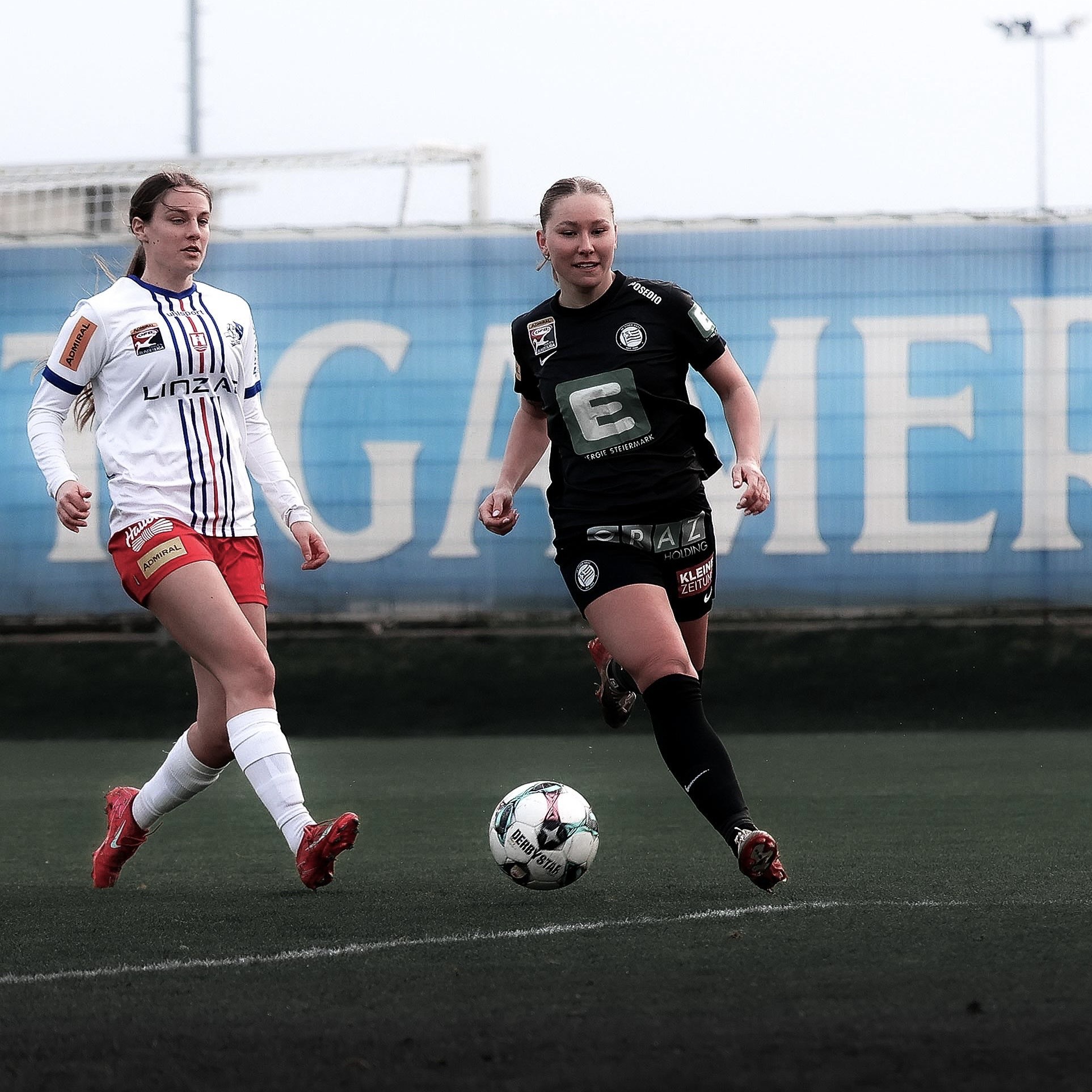 Eine Frau in schwarzem Trikot hat den Ball und eine Frau in weißem Shirt läuft hinter ihr.