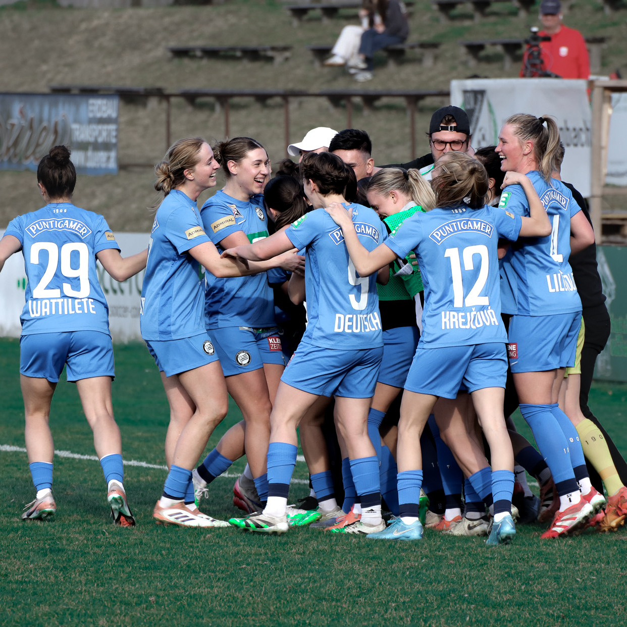 Mehrere Frauen in blauen Trikots umarmen und freuen sich.