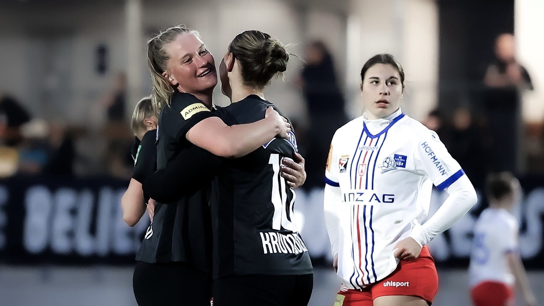 Zwei Frauen in schwarzen Trikots umarmen sich.