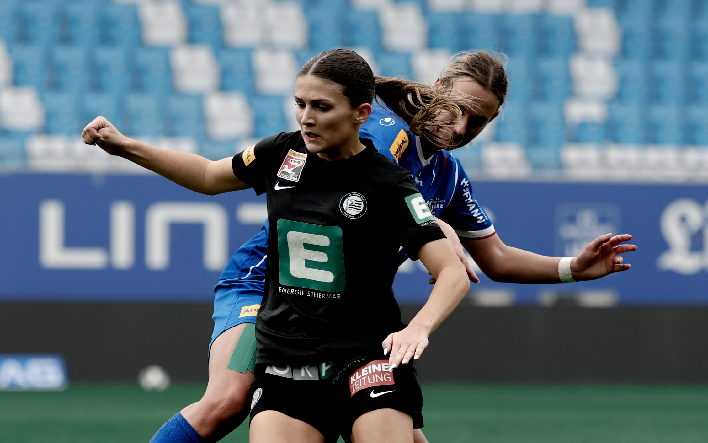 Eine Frau in schwarzem Trikot und eine Frau im blauem Trikot führen einen Zweikampf.