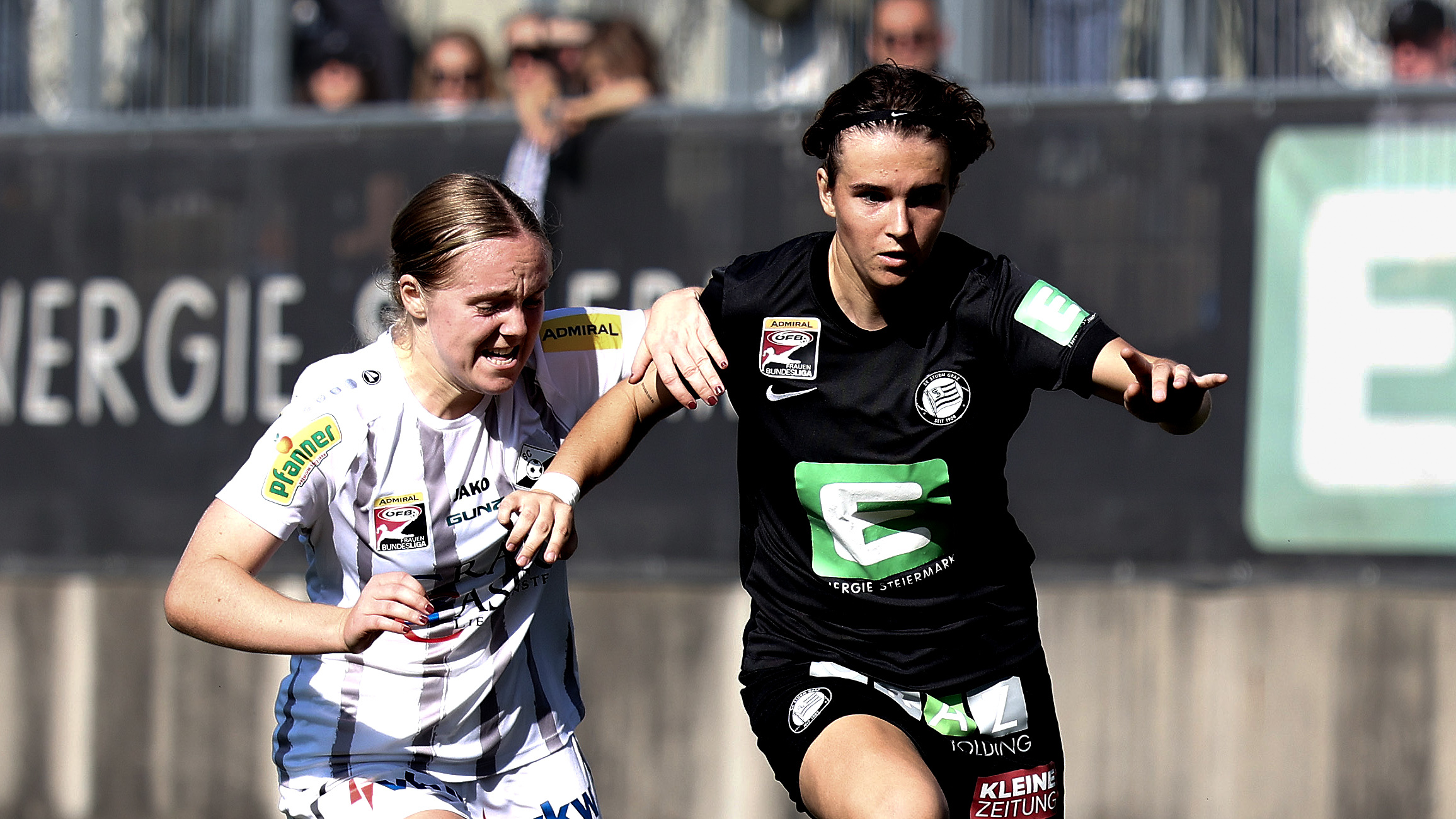 Eine Frau in schwarzen Trikot und eine Frau in weißem Trikot laufen und führen einen Zweikampf.