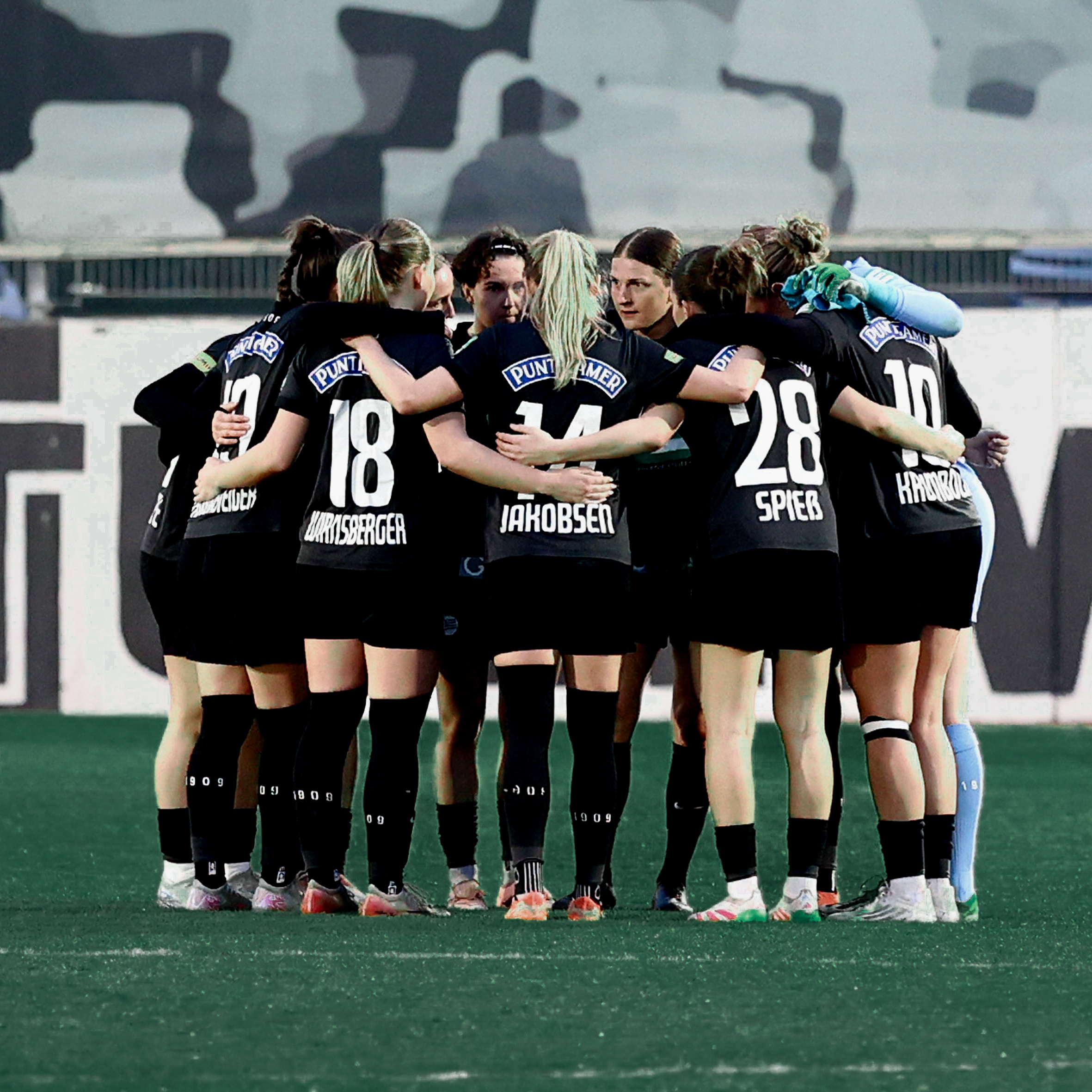 Einige Frauen in schwarzen Trikots stehen in einen Kreis und nehmen sich in den Arm,