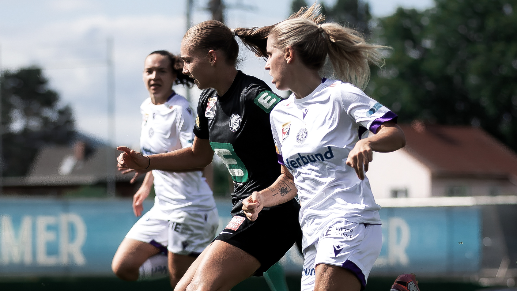 Eine Spielerin in schwarz im Zweikampf mit zwei anderen Spielerinnen in weiß