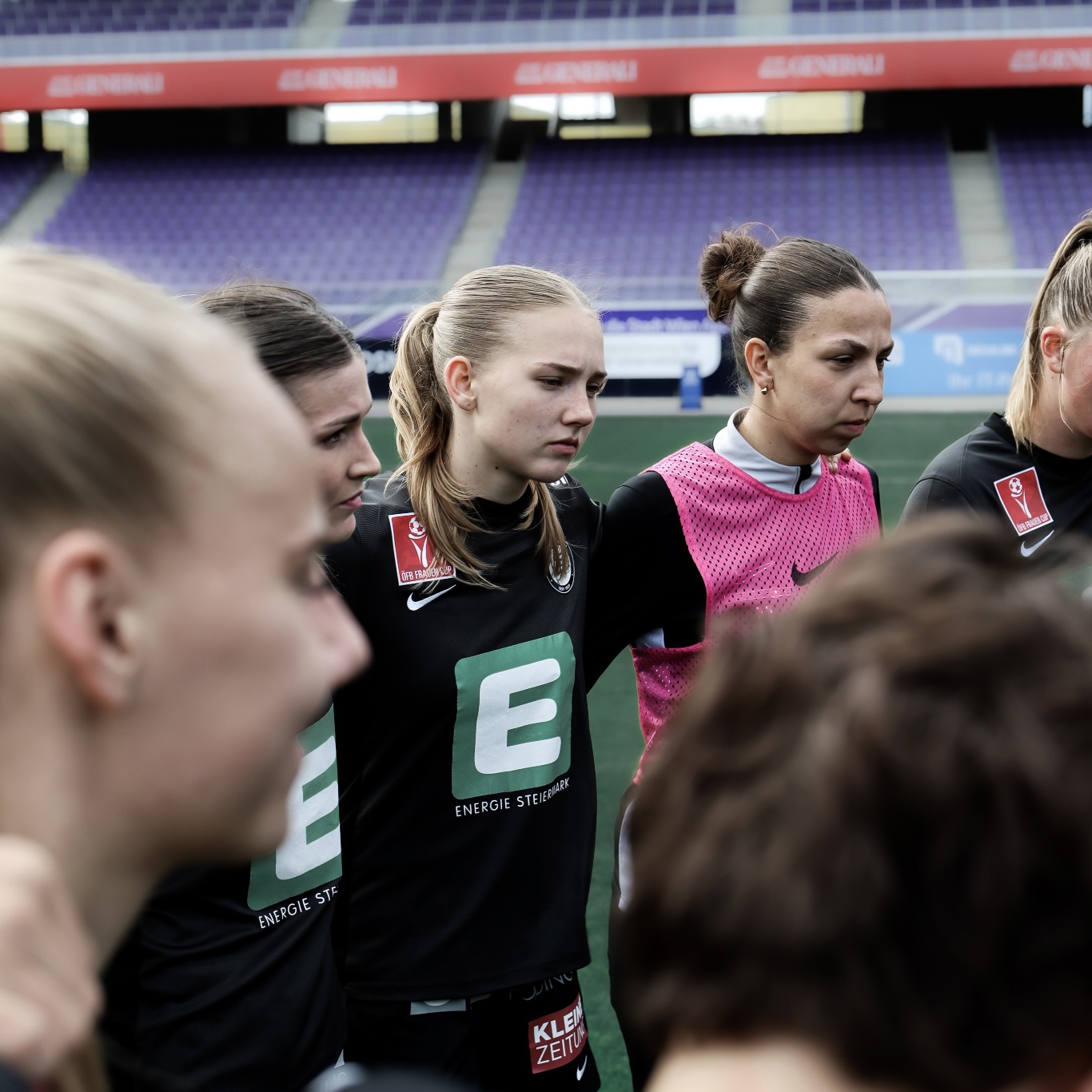 Zwei Frauen in schwarzen Trikos und eine Frau in rosa Shirt stehen zusammen.
