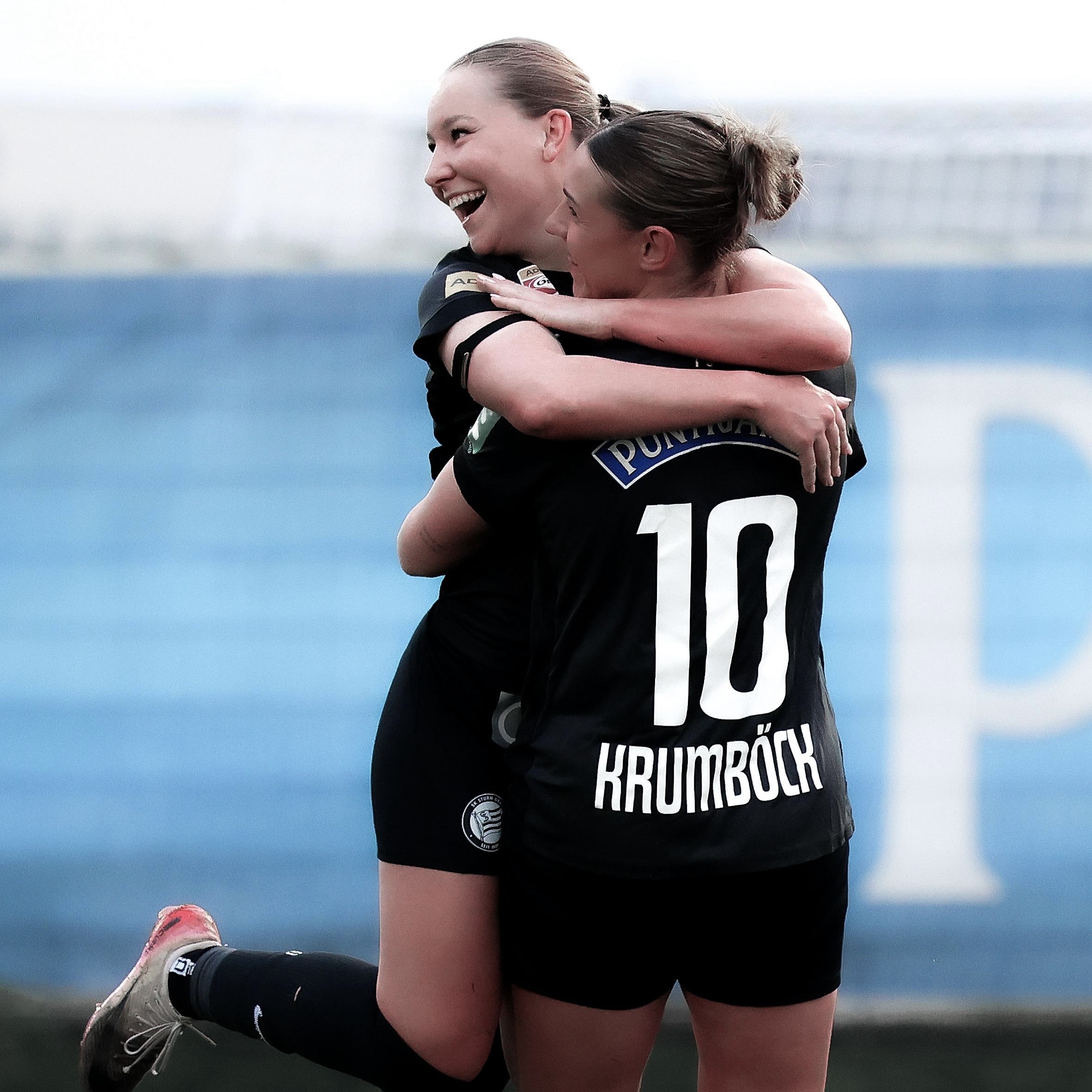 Zwei Frauen mit schwarzen Trikots umarmen sich.