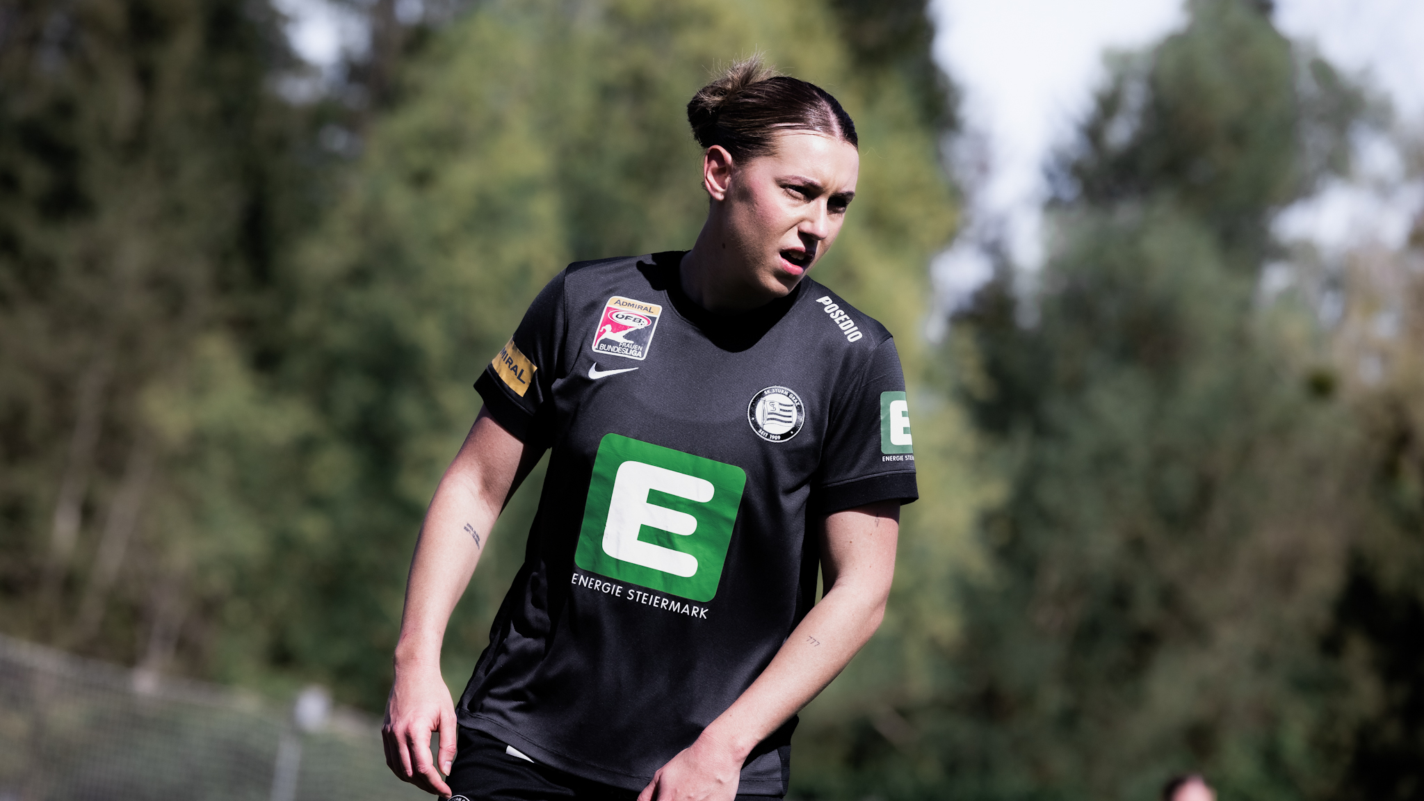 Eine Spielerin in einem schwarzen Trikot schaut in die Ferne. Es sind Bäume im Hintergrund zu sehen.