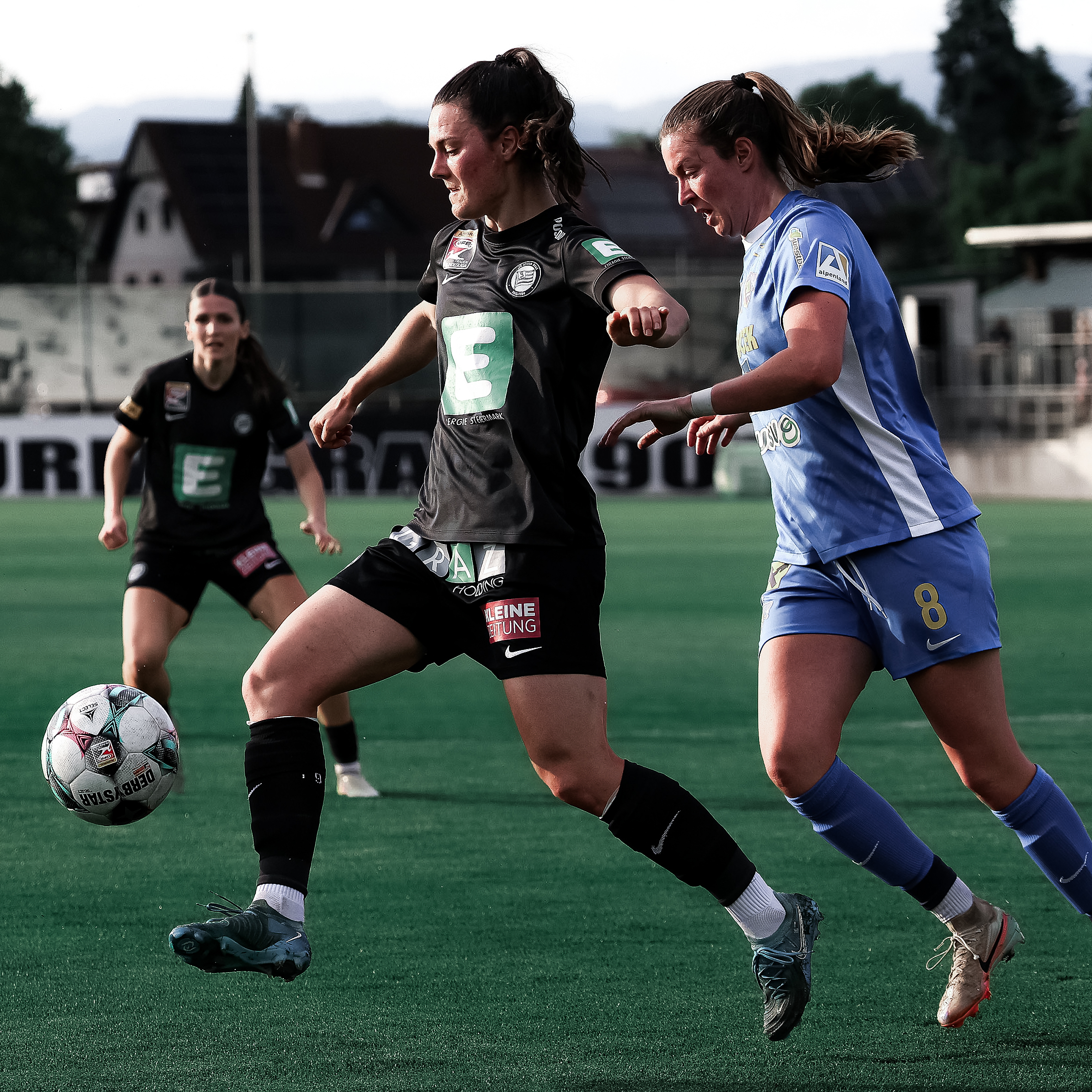 Eine Spielerin in schwarz kämpft mit einer Spielerin in blau um einen weißen Ball.