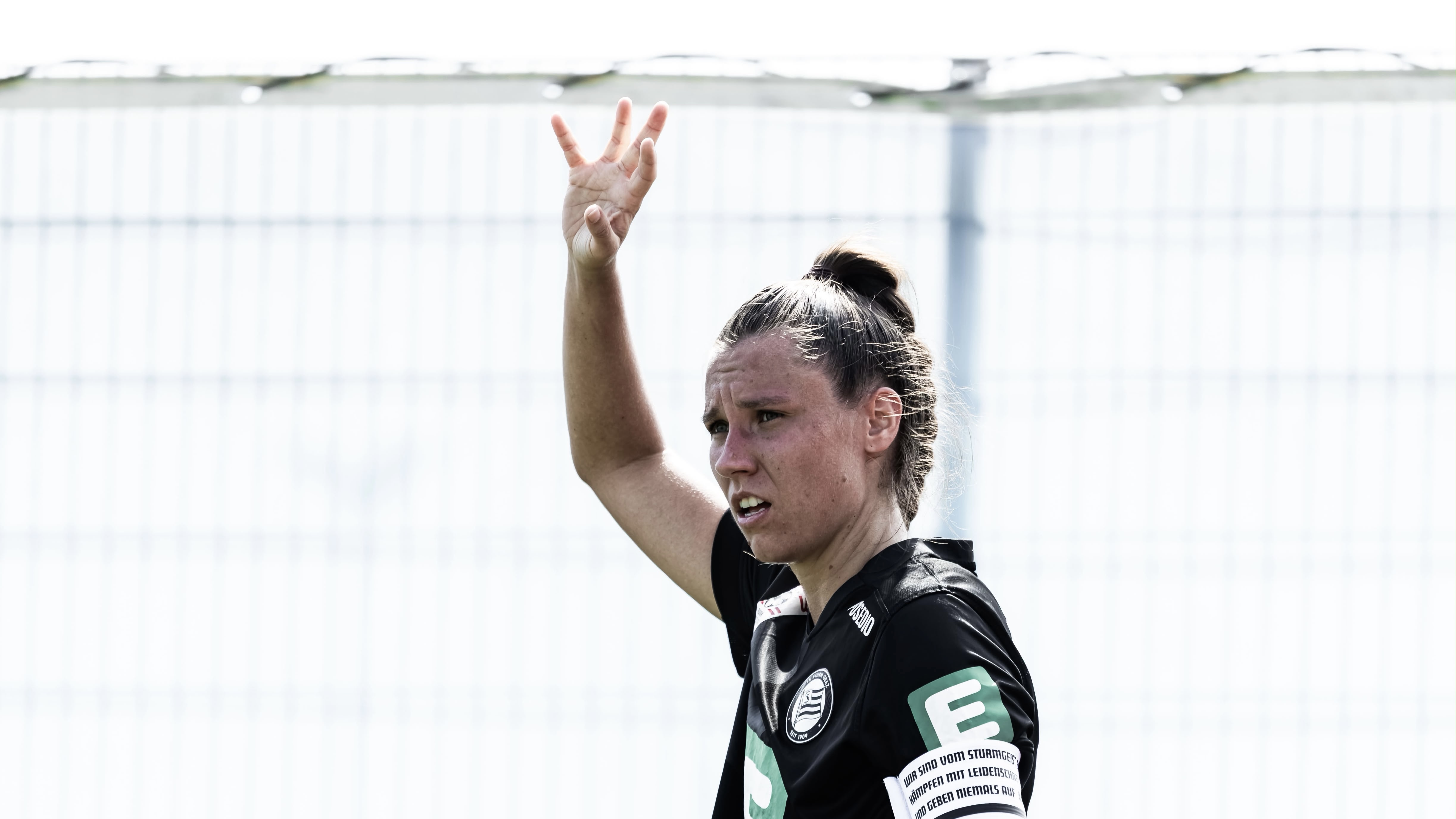 Eine Frau in schwarzem Trikot hebt die rechte Hand und schaut konzentriert.