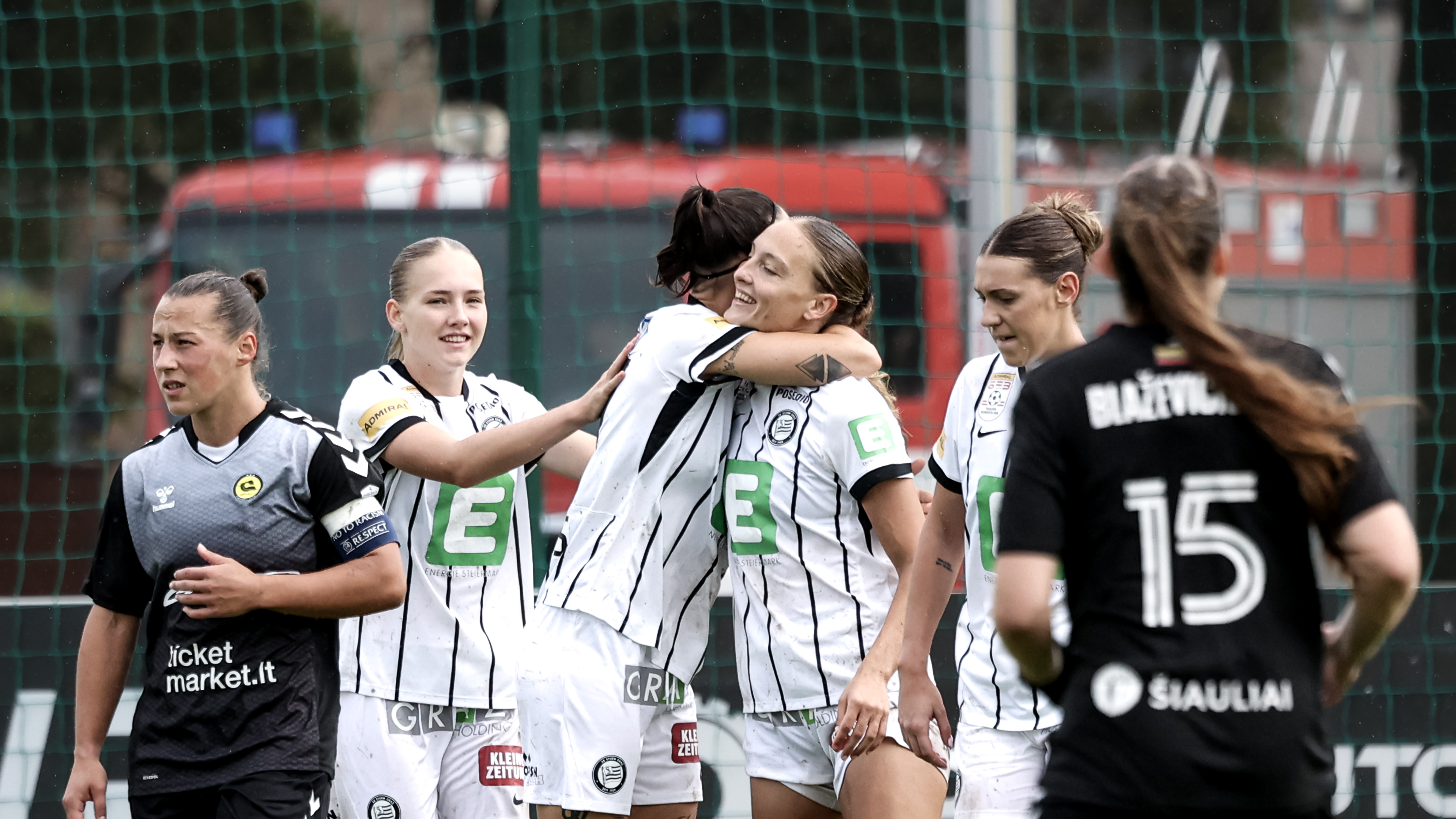 Zwei Frauen in weißen Trikots umarmen sich und zwei weitere stehen daneben.