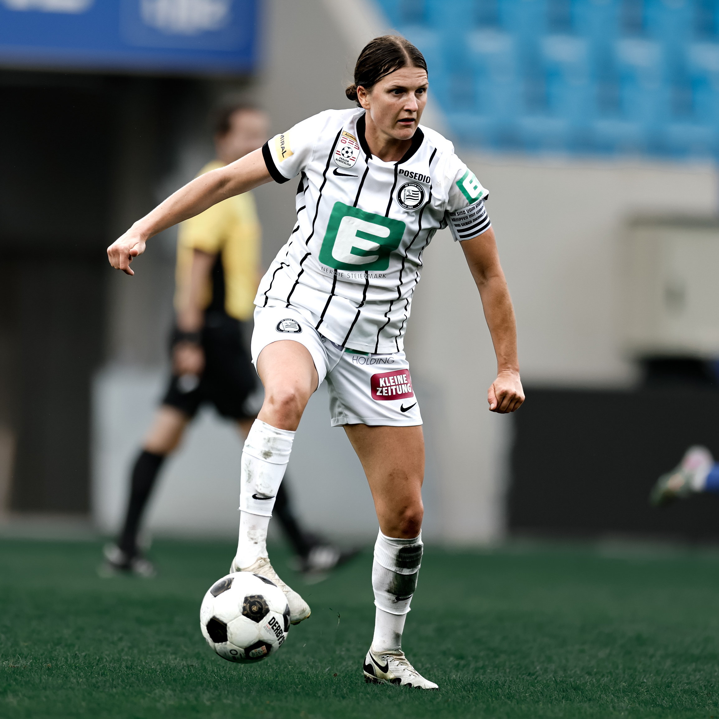 Eine Frau in weißem Trikot hat den Ball am Fuß und schaut konzentriert.