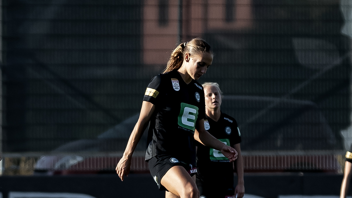 Eine Frau in schwarzen Trikot sieht zu boden.