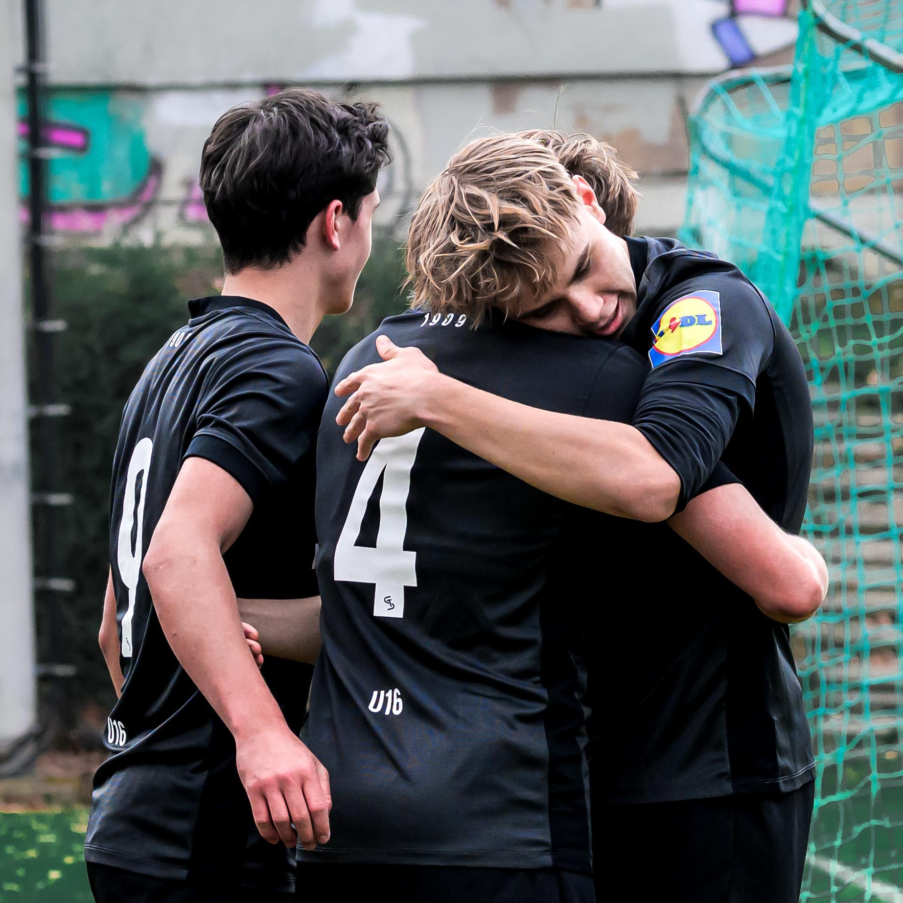 Drei Spieler in schwarz jubeln und umarmen sich