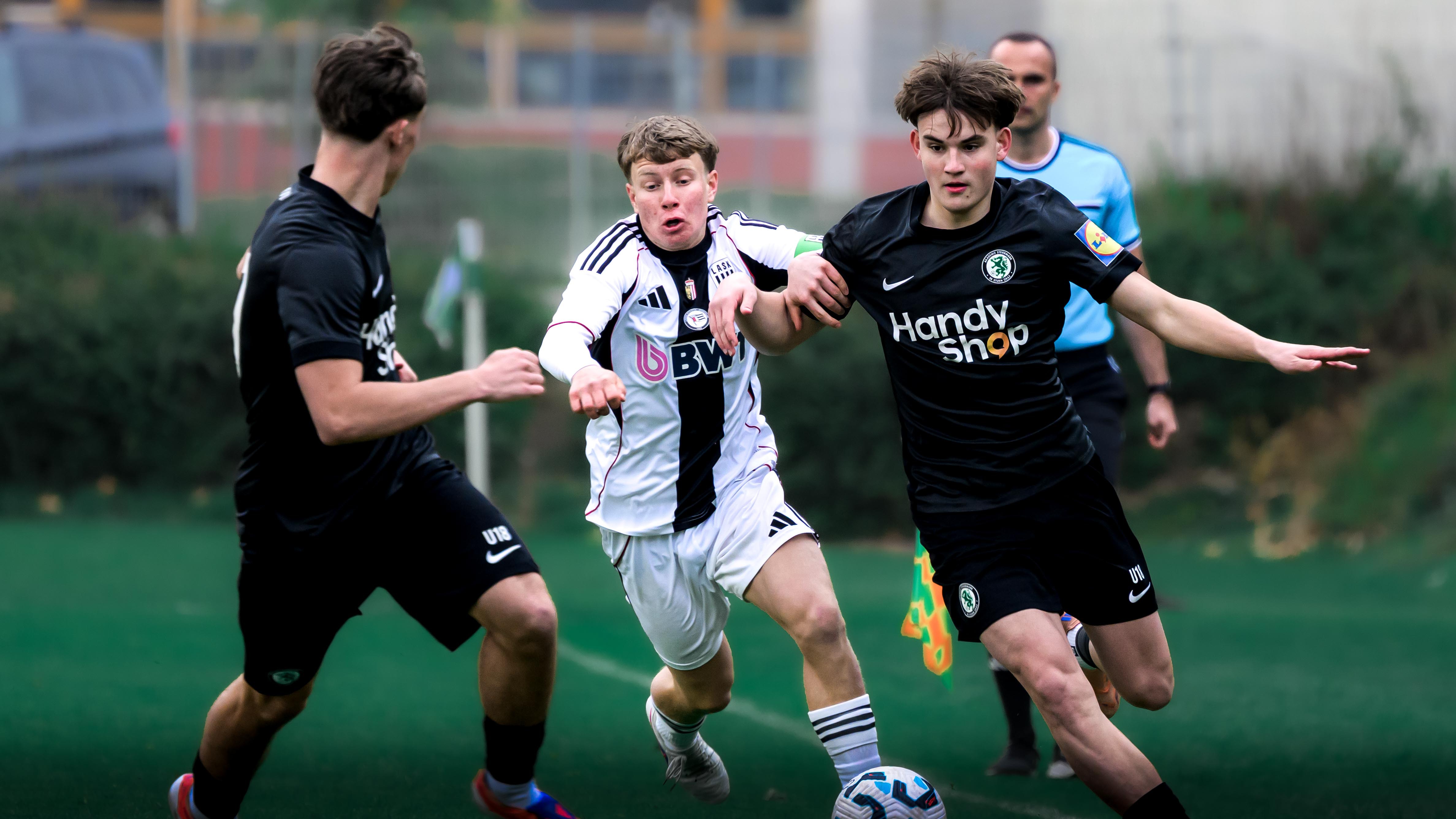 Zwei Spieler in schwarz und einer in weiß kämpfen um den Ball