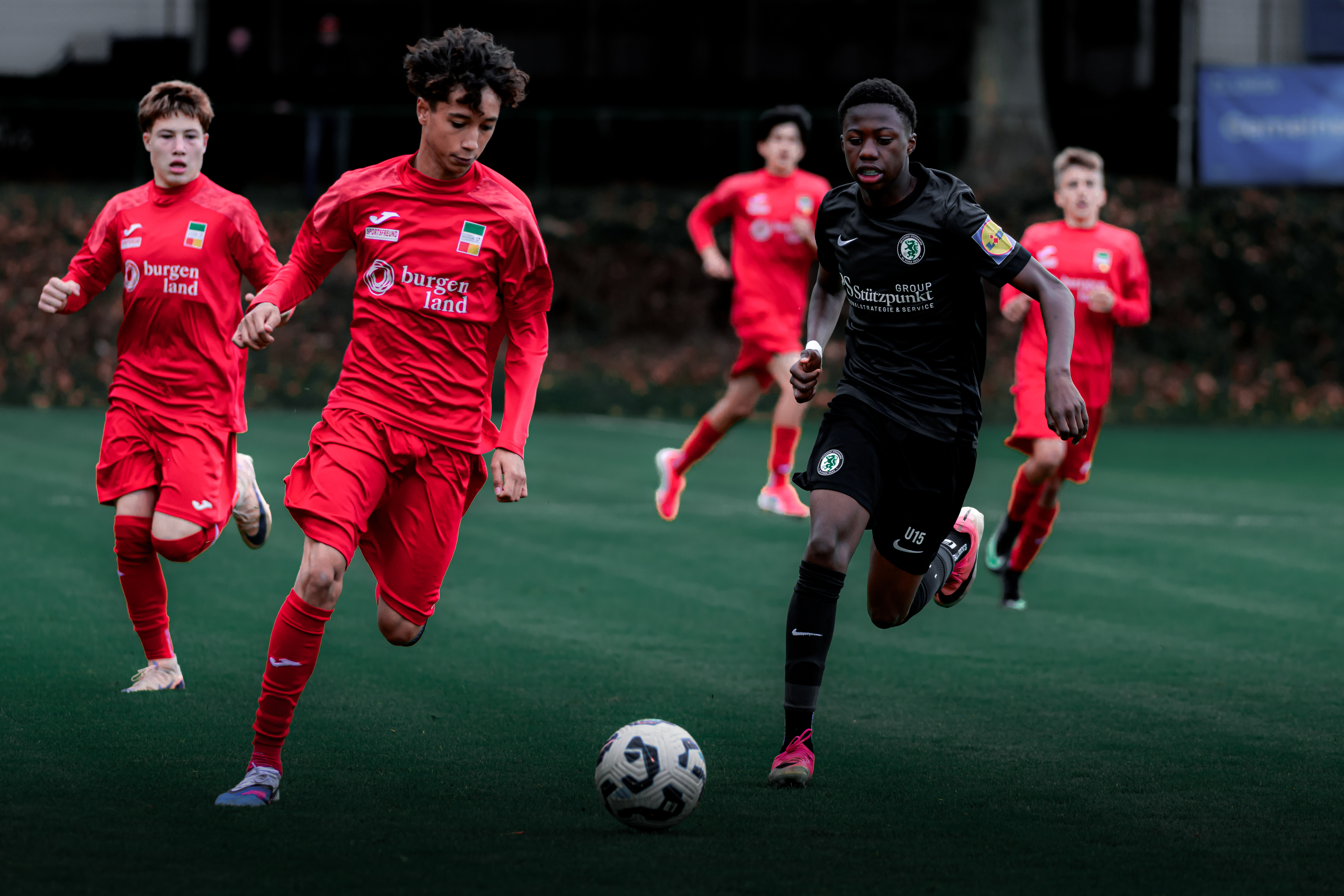 Zwei Spieler kämpfen um einen Ball, einer ist schwarz gekleidet, der andere rot.