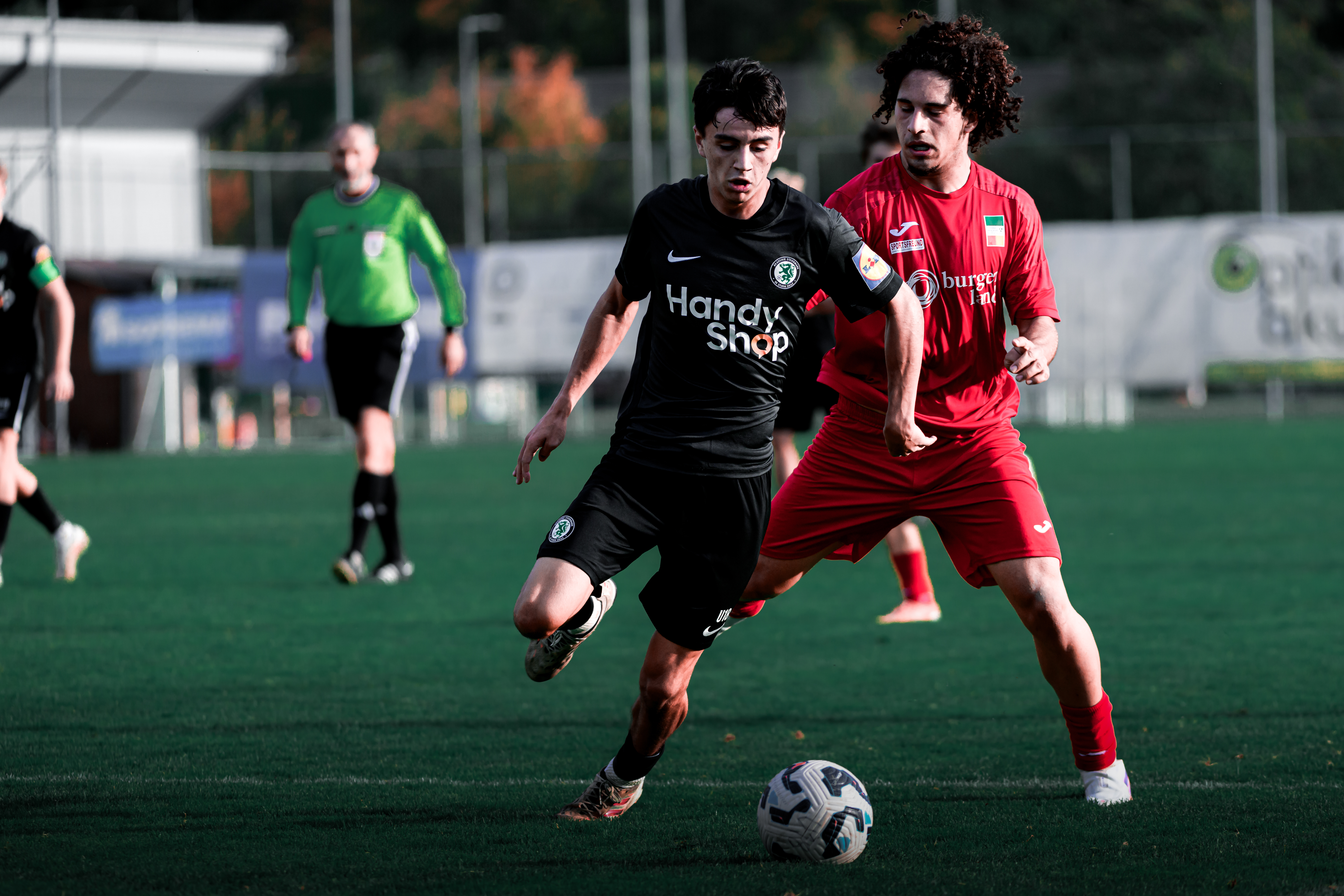 Zwei Spieler kämpfen um einen Ball, einer ist schwarz gekleidet, der andere rot.