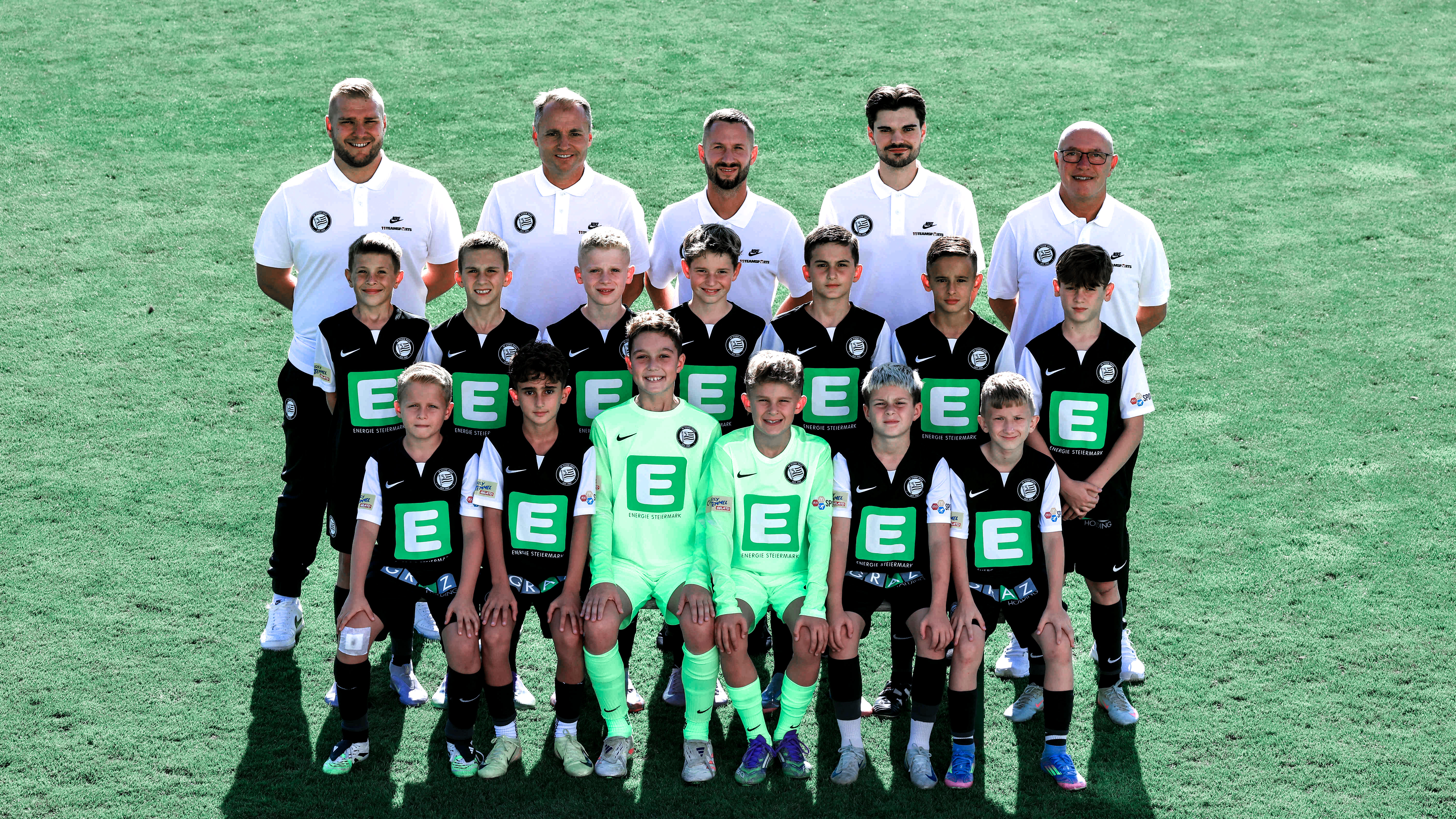 Viele Kinder in schwarzen Trikots stehen in mehreren Reihen und einige erwachsene Trainer haben weiße Shirts an