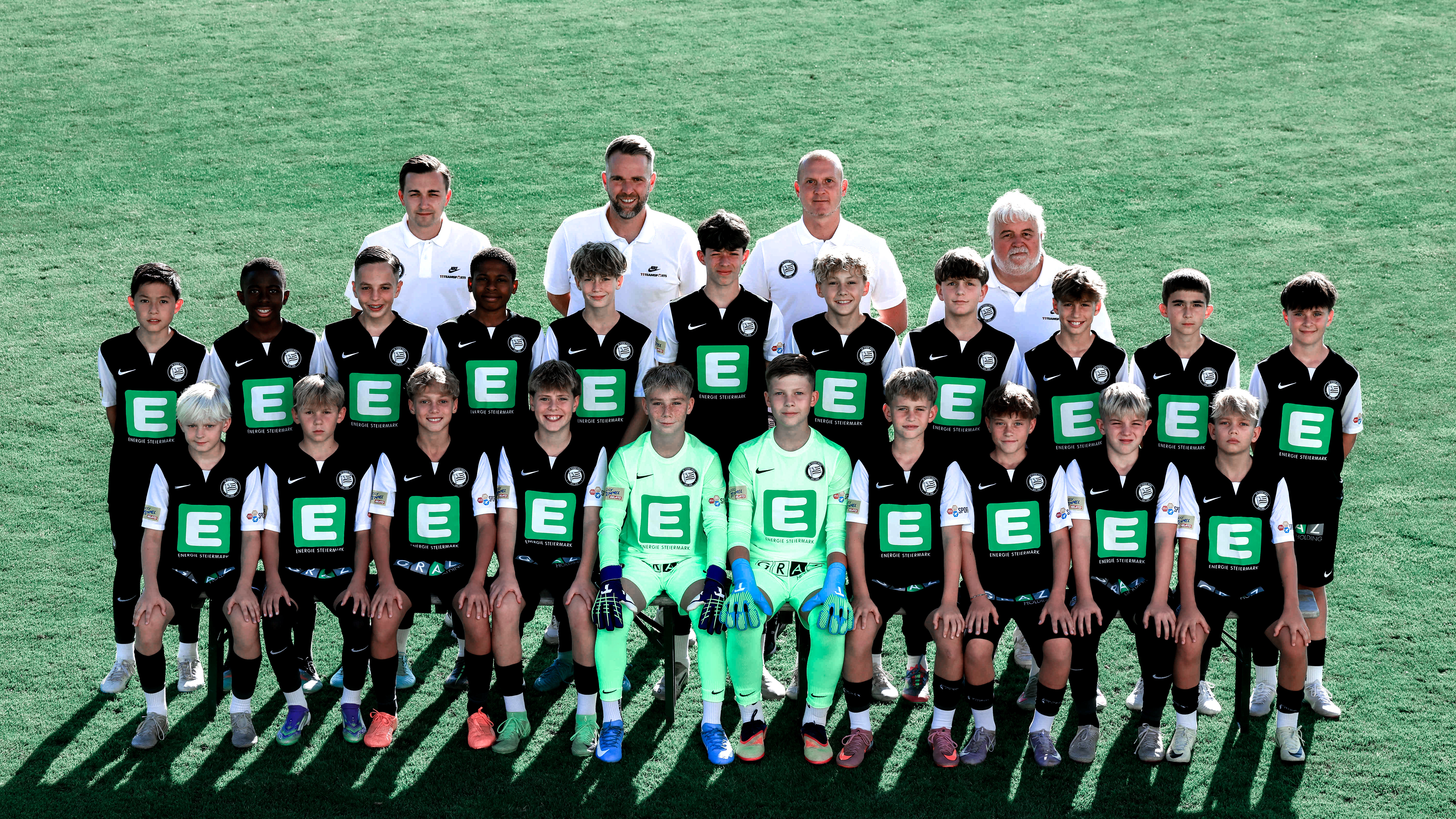 Viele Kinder in schwarzen Trikots stehen in mehreren Reihen und einige erwachsene Trainer haben weiße Shirts an