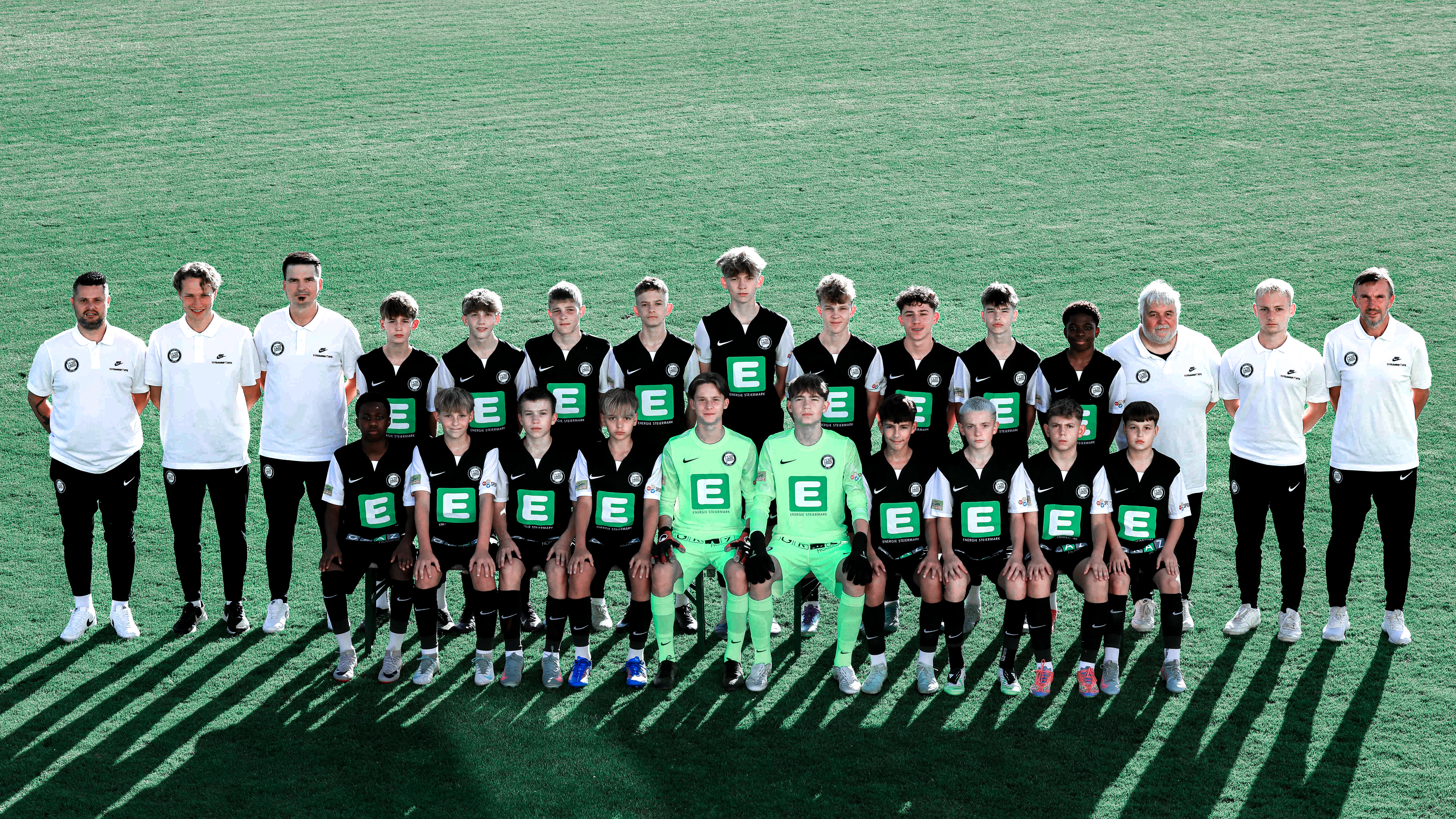 Viele Kinder in schwarzen Trikots stehen in mehreren Reihen und einige erwachsene Trainer haben weiße Shirts an