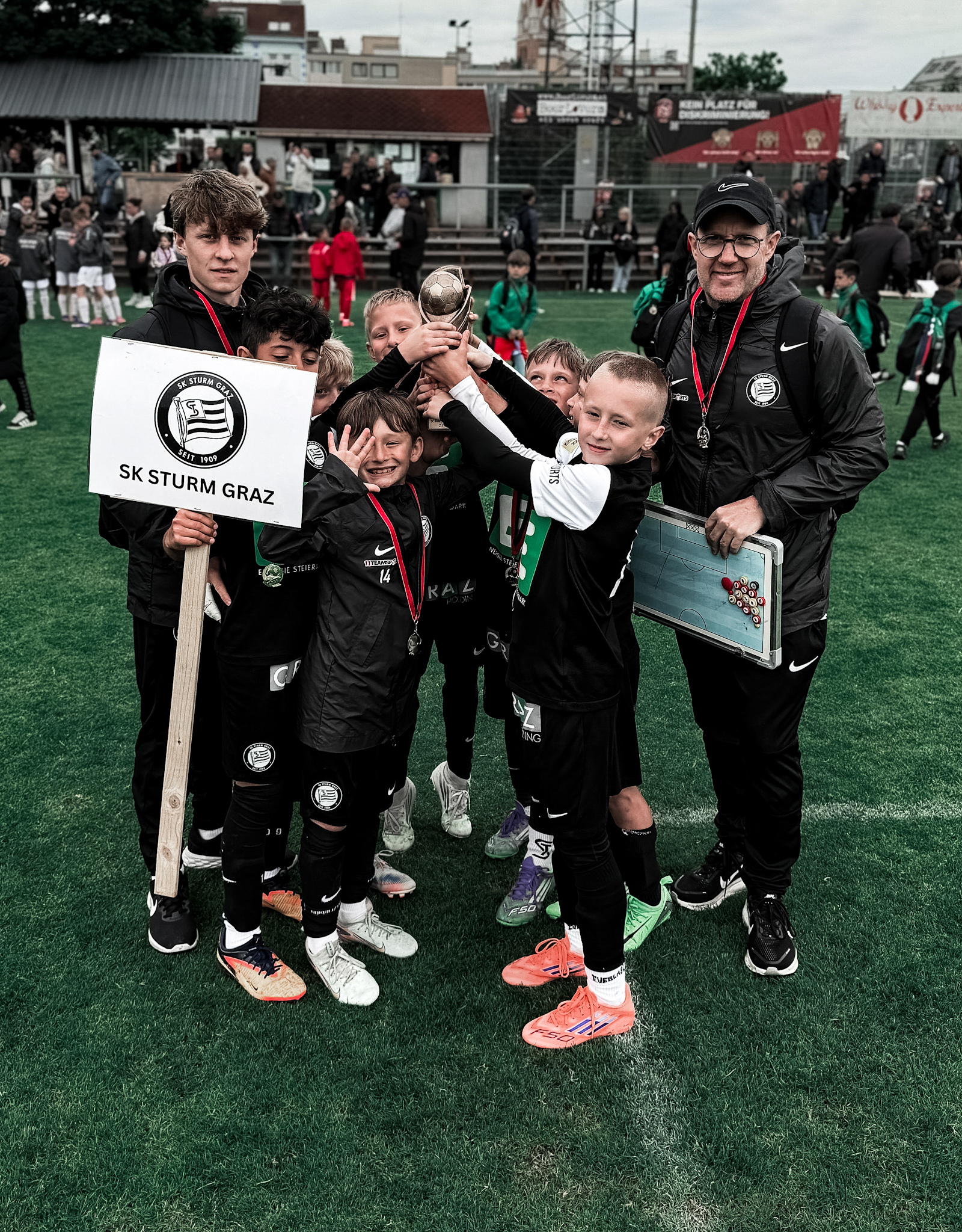 Viele junge Spieler halten einen Pokal hoch, zwei Trainer stehen seitlich dahinter