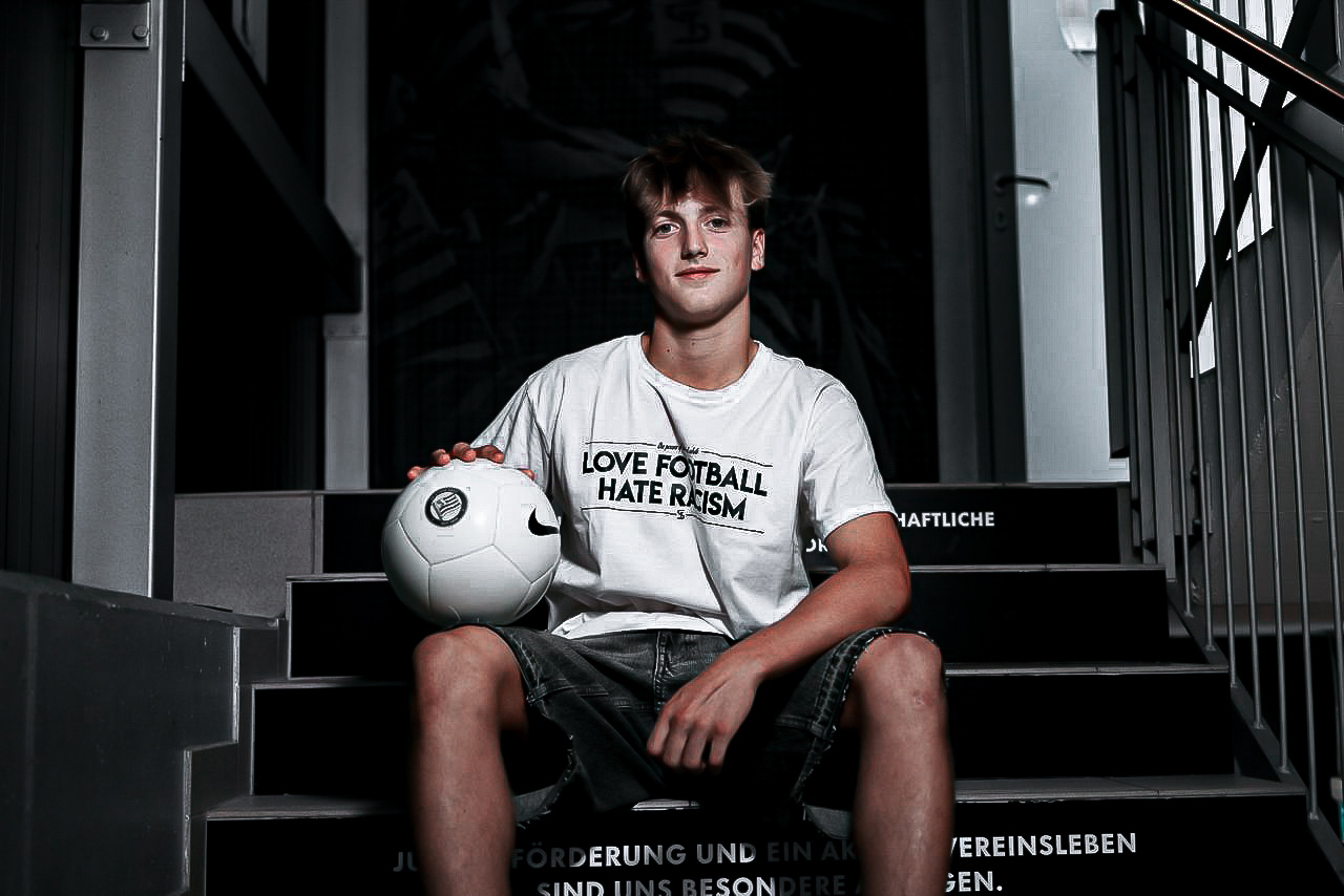 Ein junger Mann sitzt mit Ball auf einer Stiege.