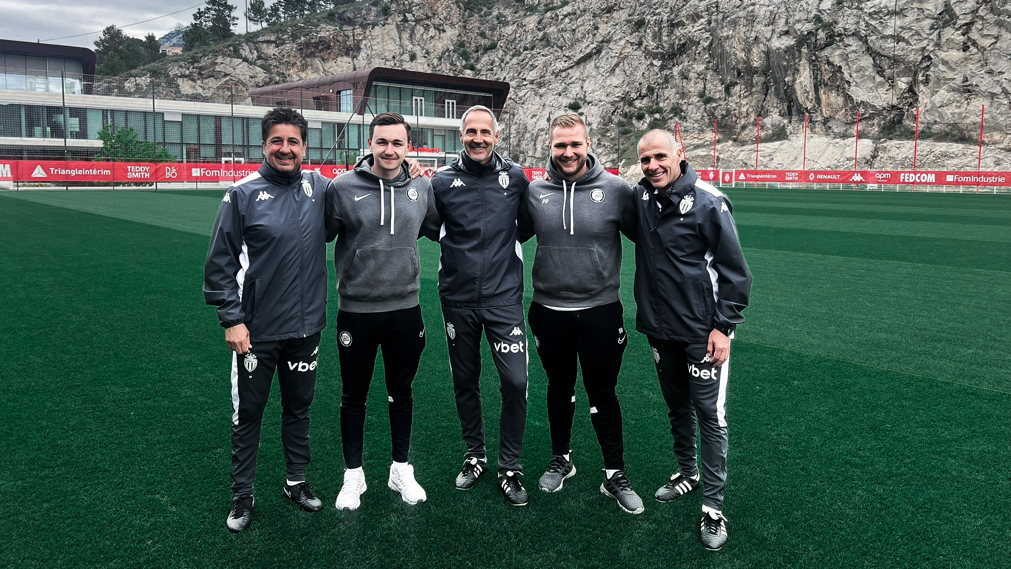 Fünf Männer in Trainingskleidung auf einem Fußballplatz.